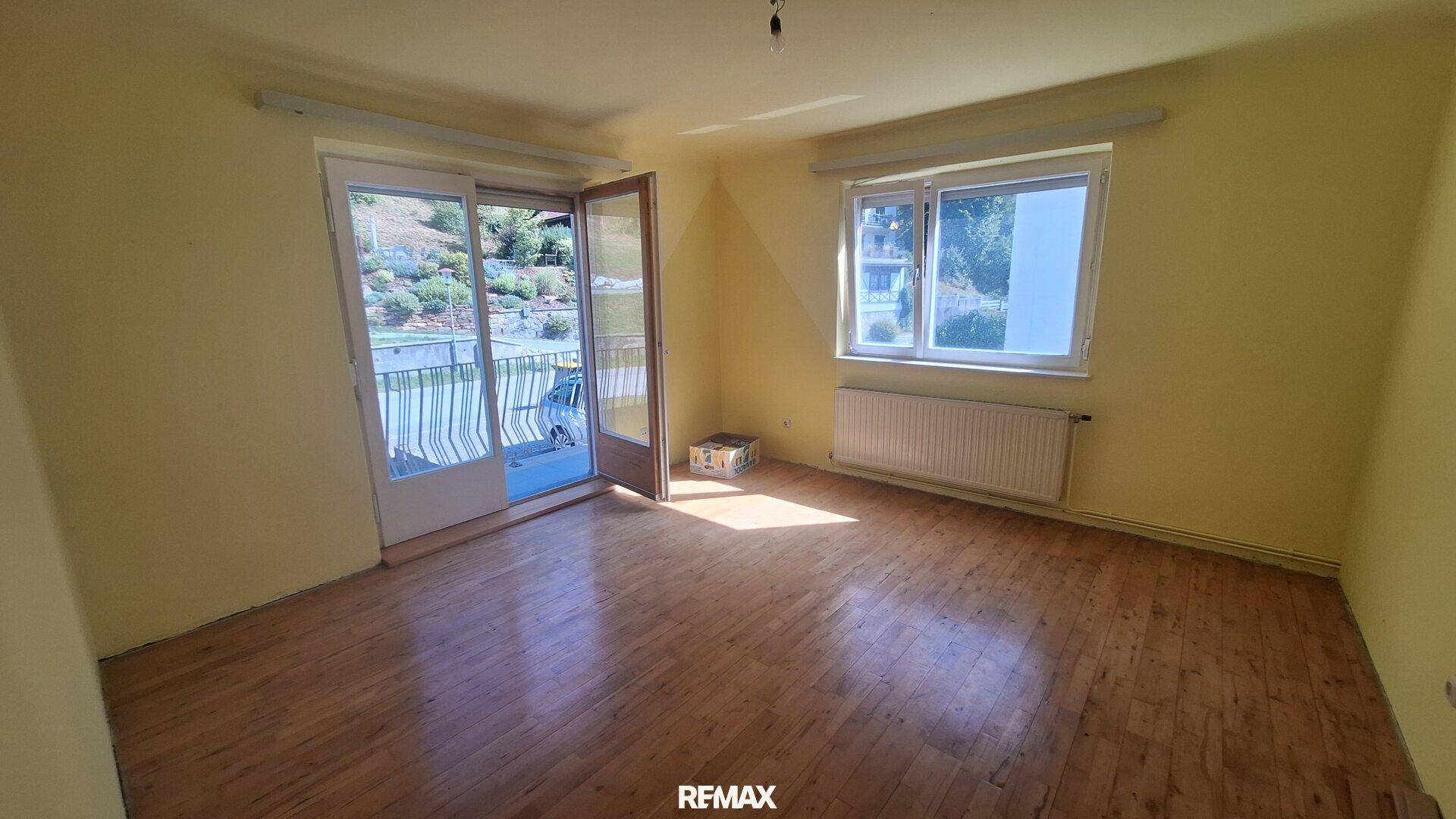 Helles Wohnzimmer mit Holzboden und Zugang zu einem Balkon mit Blick ins Grüne.
