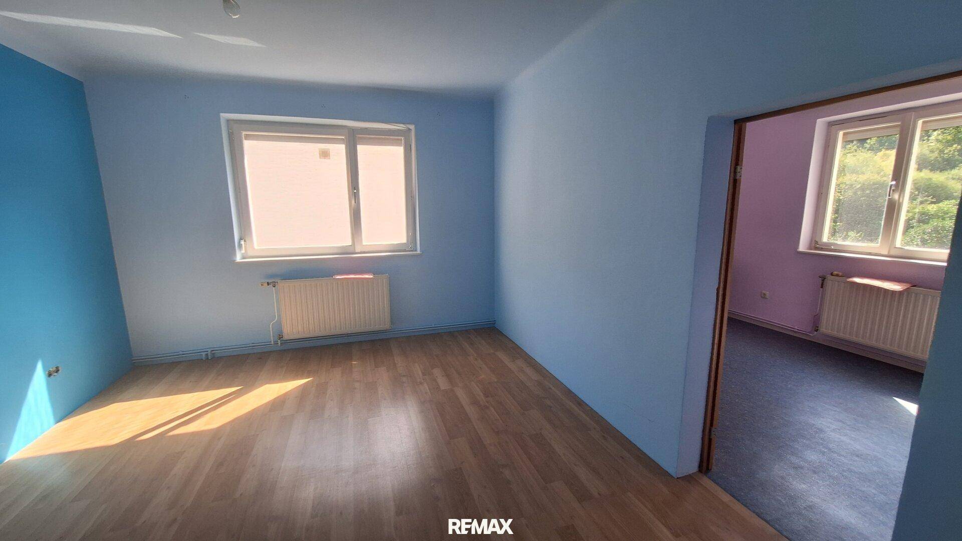 Schlafzimmer mit blau gestrichenen Wänden, Holzboden und Heizkörper unter dem Fenster.
