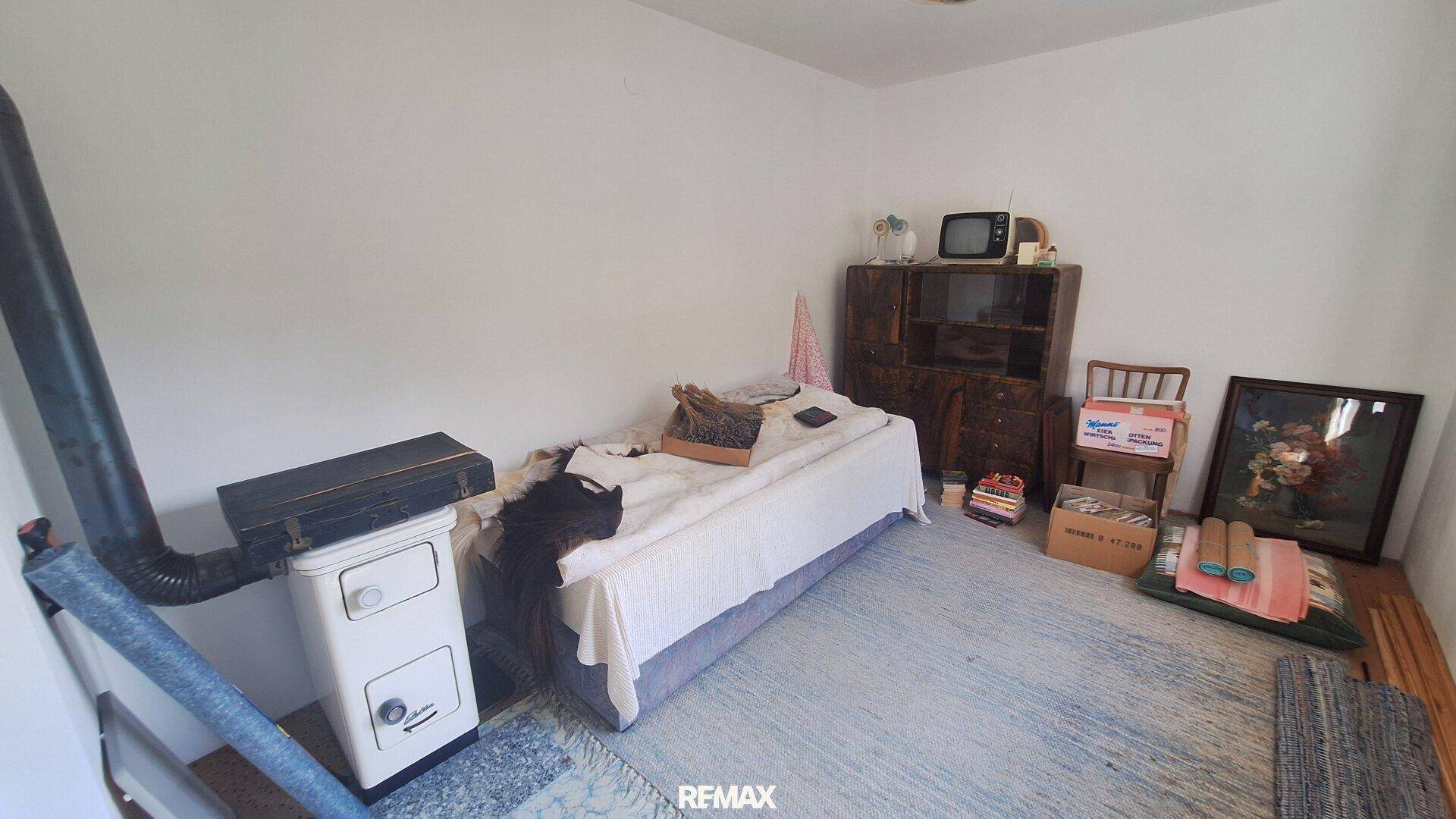 Schlafzimmer mit weiß gestrichenen Wänden, Teppichboden und einem traditionellen Holzofen.