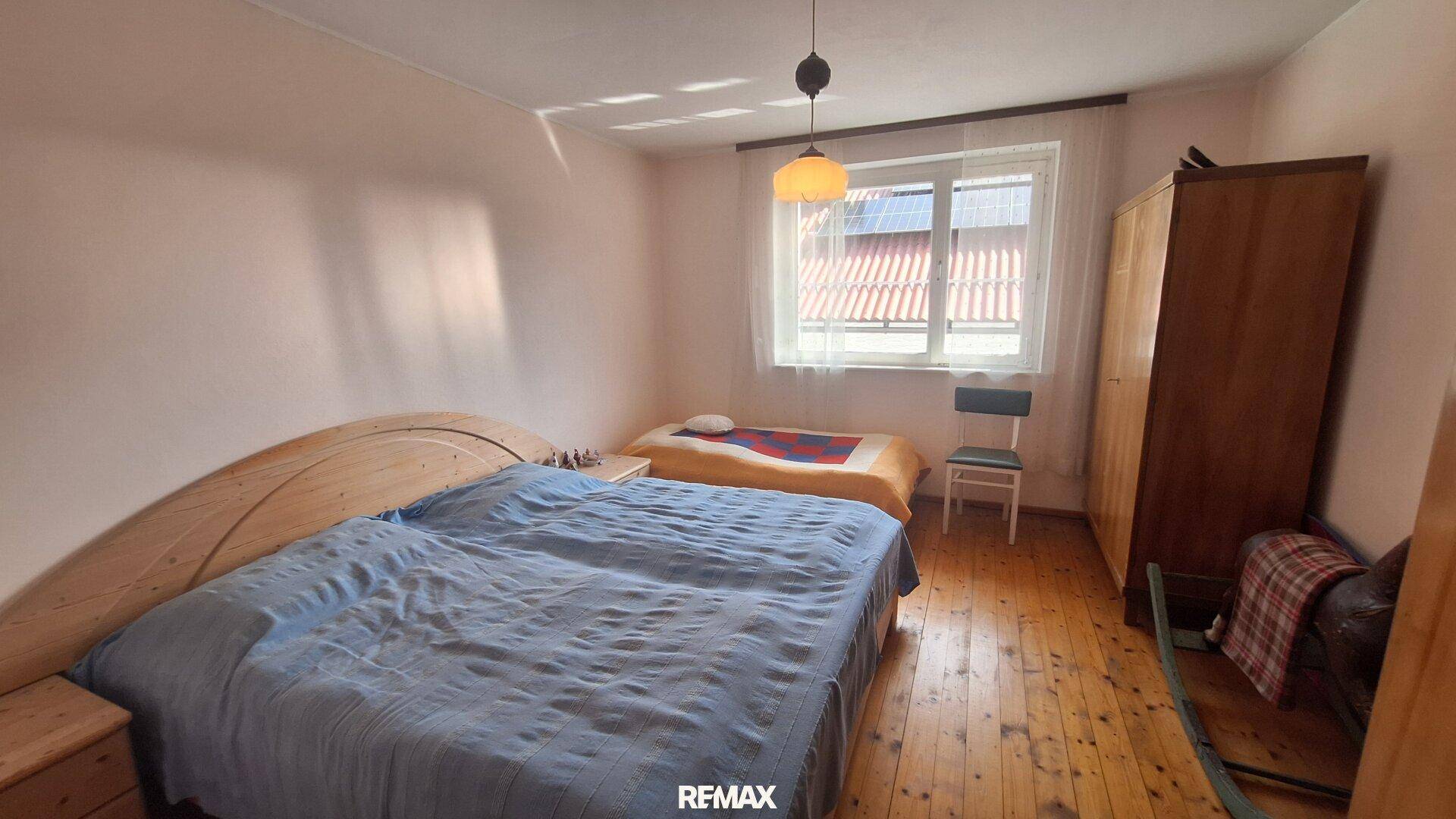 Schlafzimmer mit Holzboden, Doppelbett und Fenster mit Blick auf ein rotes Dach.