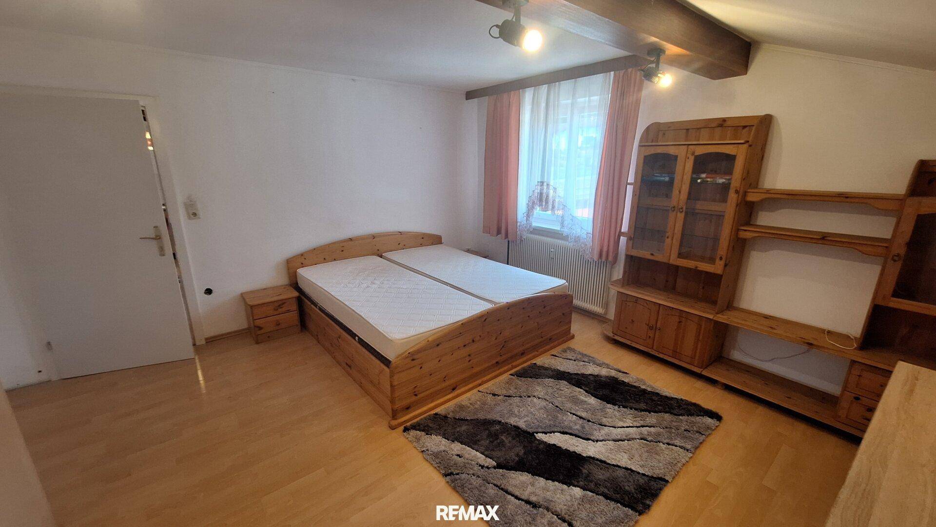 Helles Schlafzimmer mit Doppelbett, Holzbalken und rustikalen Holzmöbeln im Dachgeschoss.
