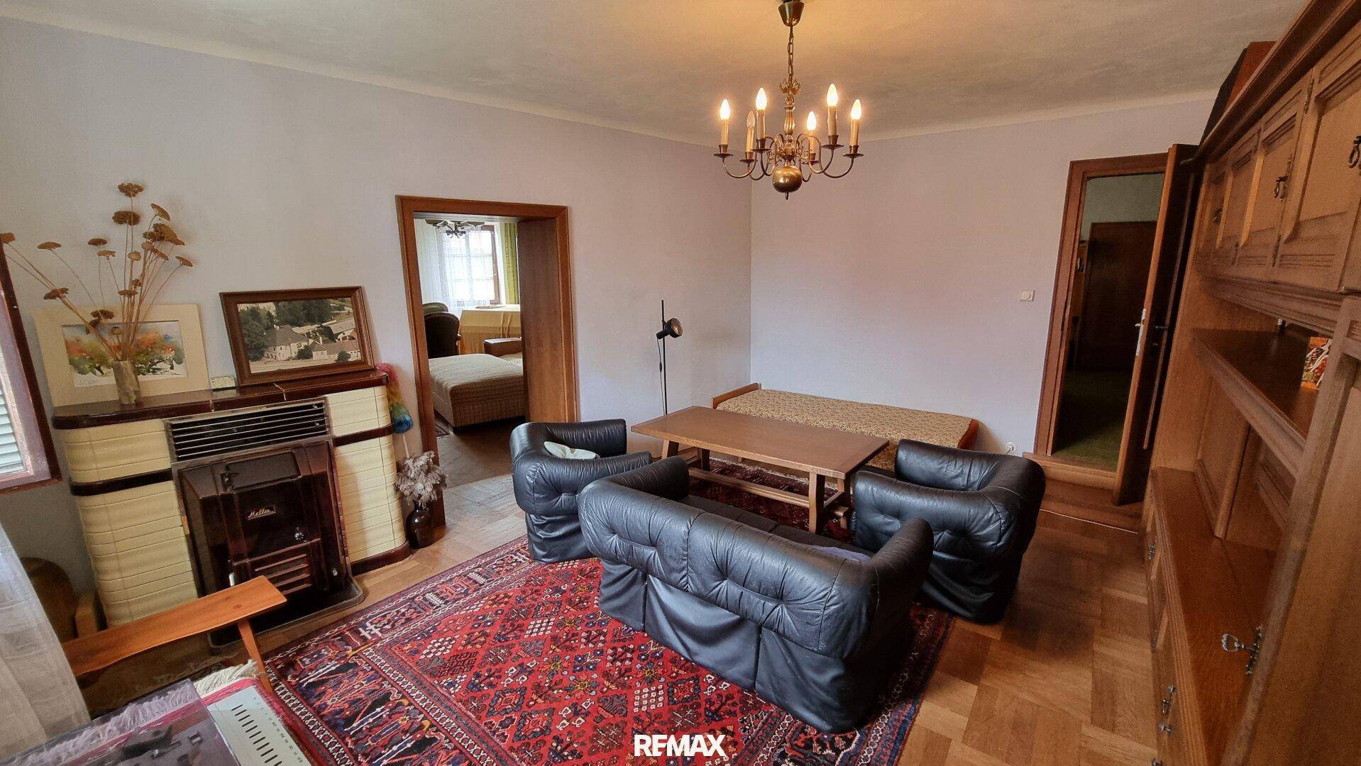 Gemütliches Wohnzimmer mit traditionellem Kachelofen, dunklen Ledersesseln und Parkettboden.