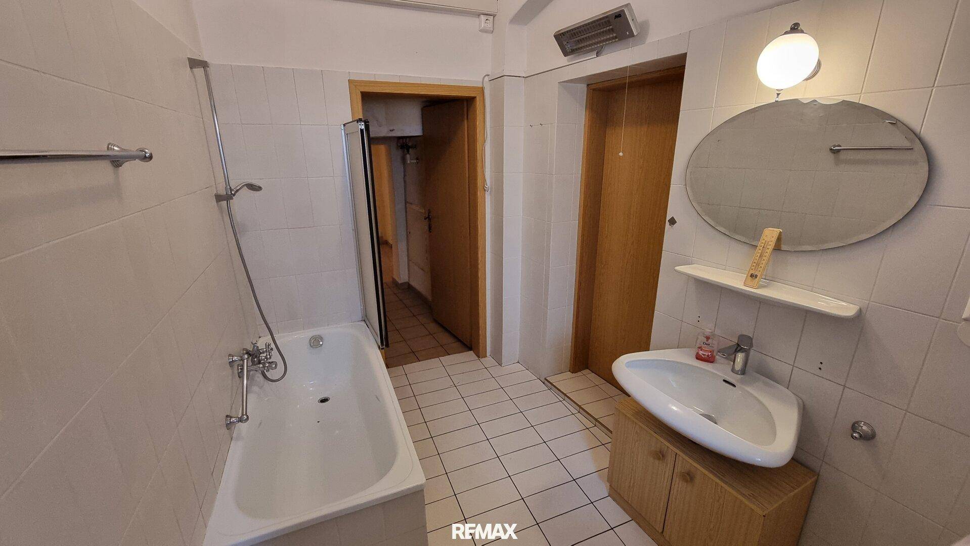 Helles Badezimmer mit Badewanne, Waschbecken und weißen Fliesen, in gutem Zustand.