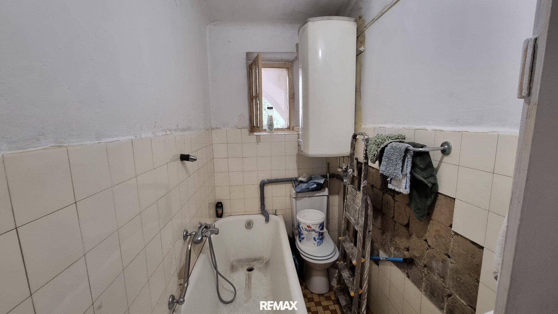 Einfaches Badezimmer mit Badewanne, Toilette und Boiler, teilweise renovierungsbedürftig.