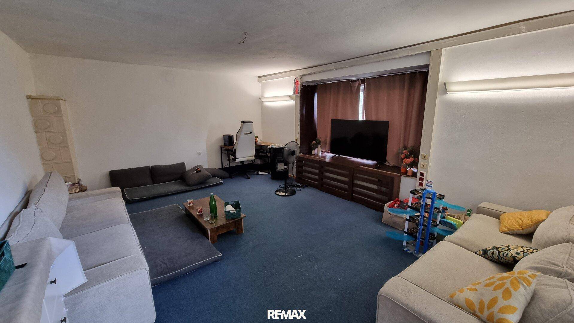 Geräumiges Wohnzimmer mit blauem Teppichboden, bequemen Sofas und Unterhaltungselektronik.