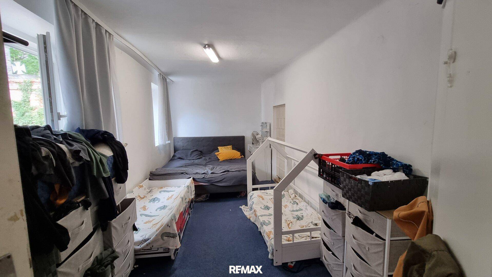 Schlafzimmer mit mehreren Betten, weiß gestrichenen Wänden und einfachem Mobiliar.