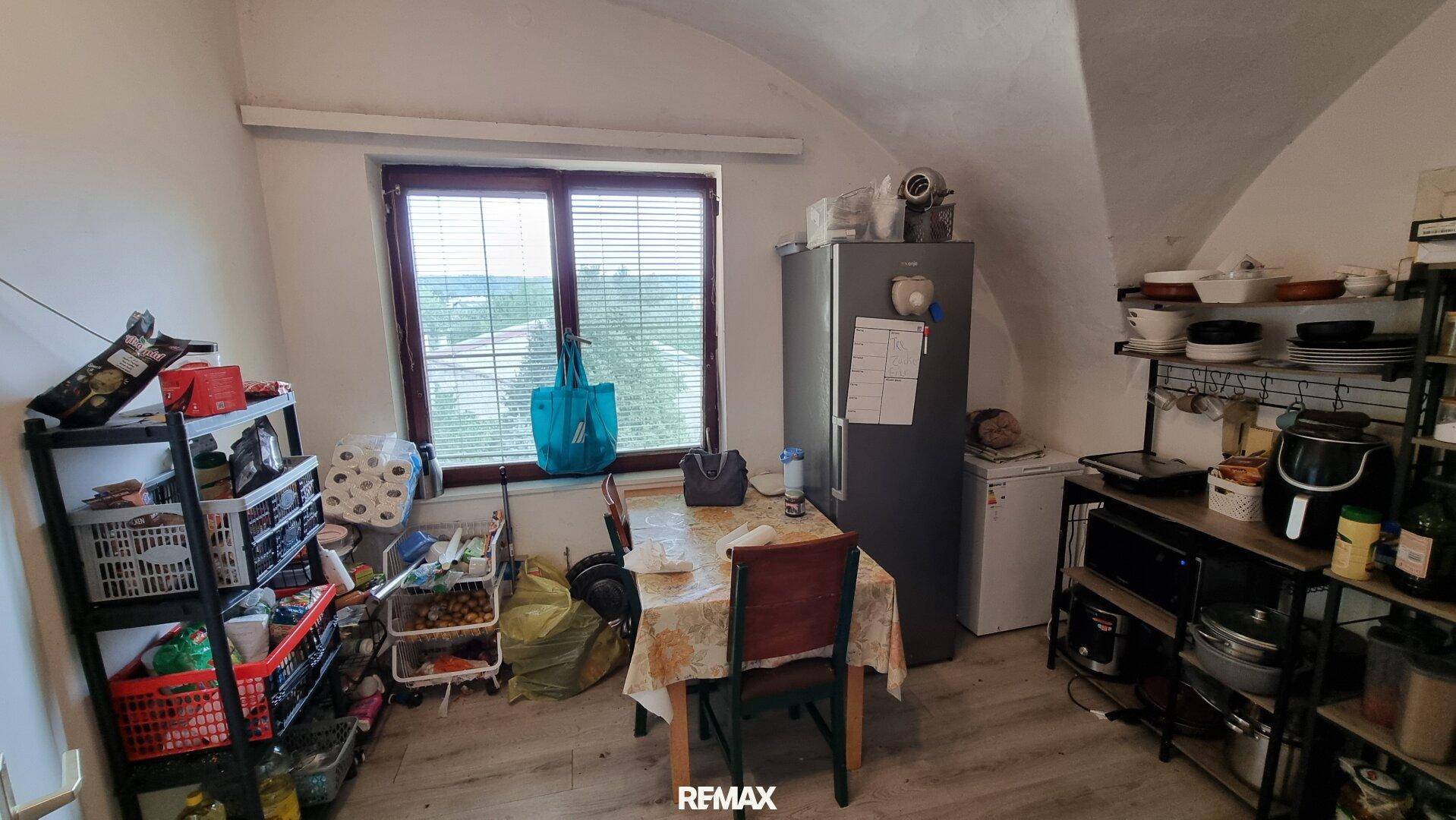 Dachgeschossraum mit Esstisch, Kühlschrank und Regalen, unter einer Dachschräge gelegen.