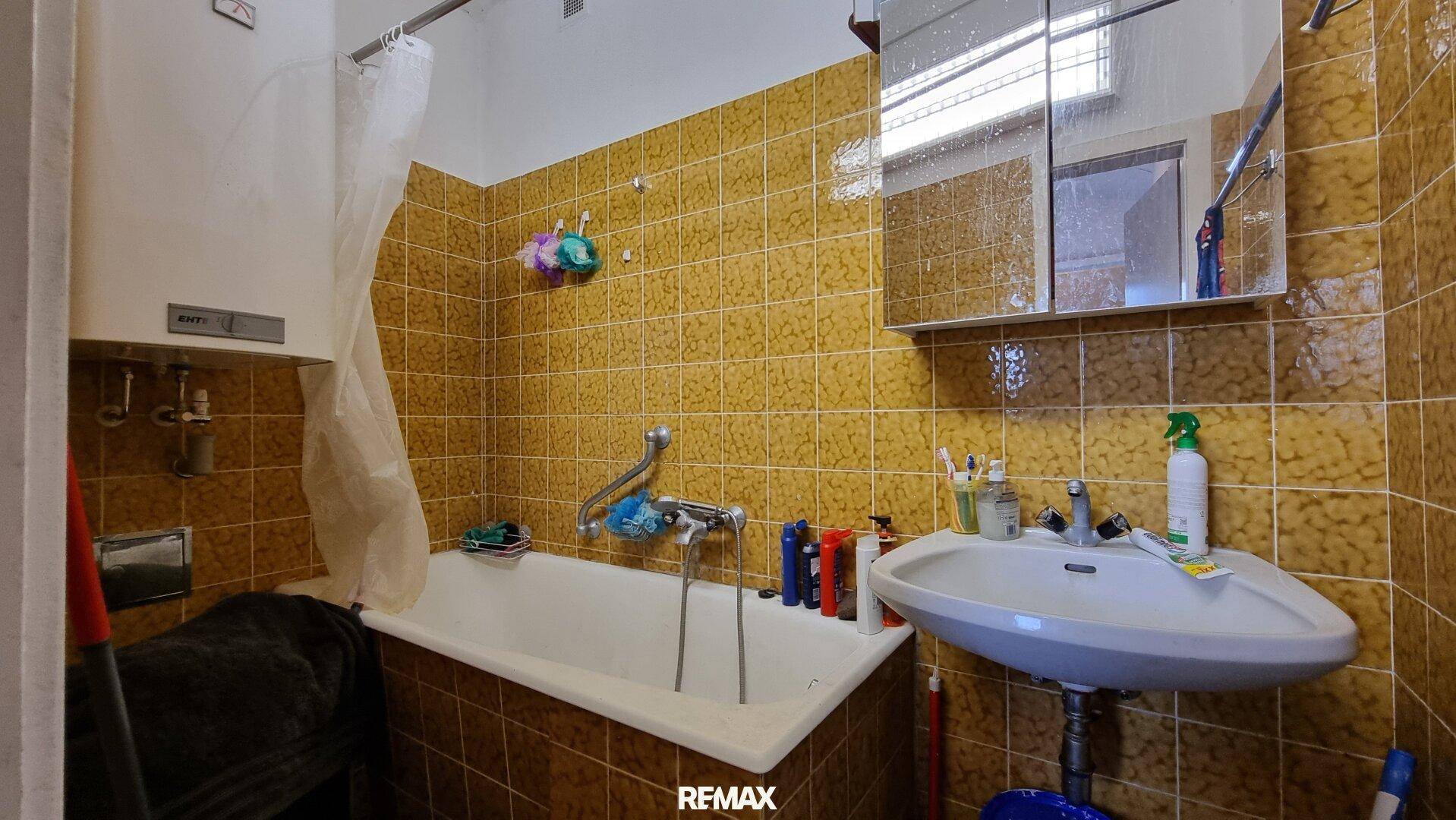 Badezimmer mit gelben Fliesen, Badewanne und Waschbecken, im Stil der 80er Jahre.