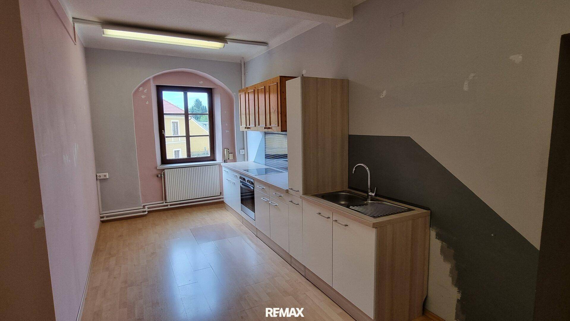 Einfache Küchenzeile mit Spüle und Herd, in einem Raum mit Holzboden und Fenster.