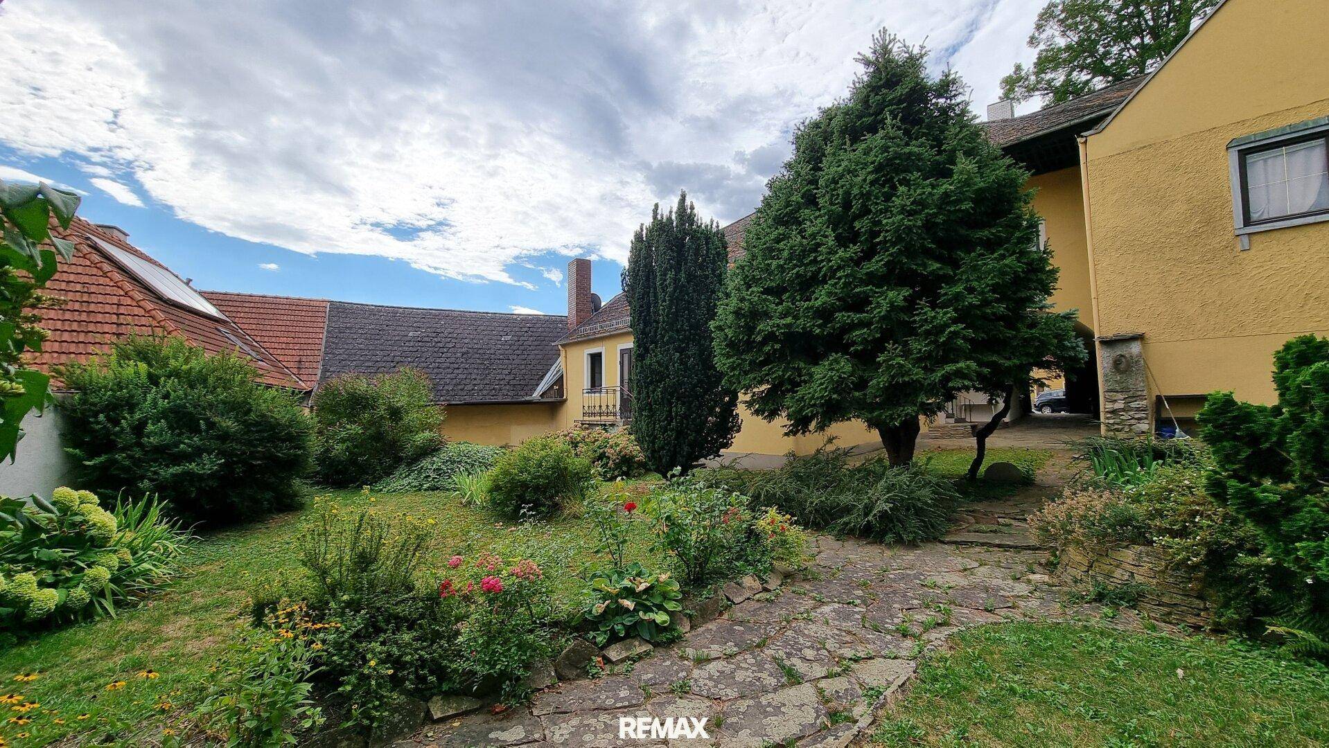 Gepflegter Gartenbereich mit altem Baumbestand und einem traditionellen Gebäude im Hintergrund.