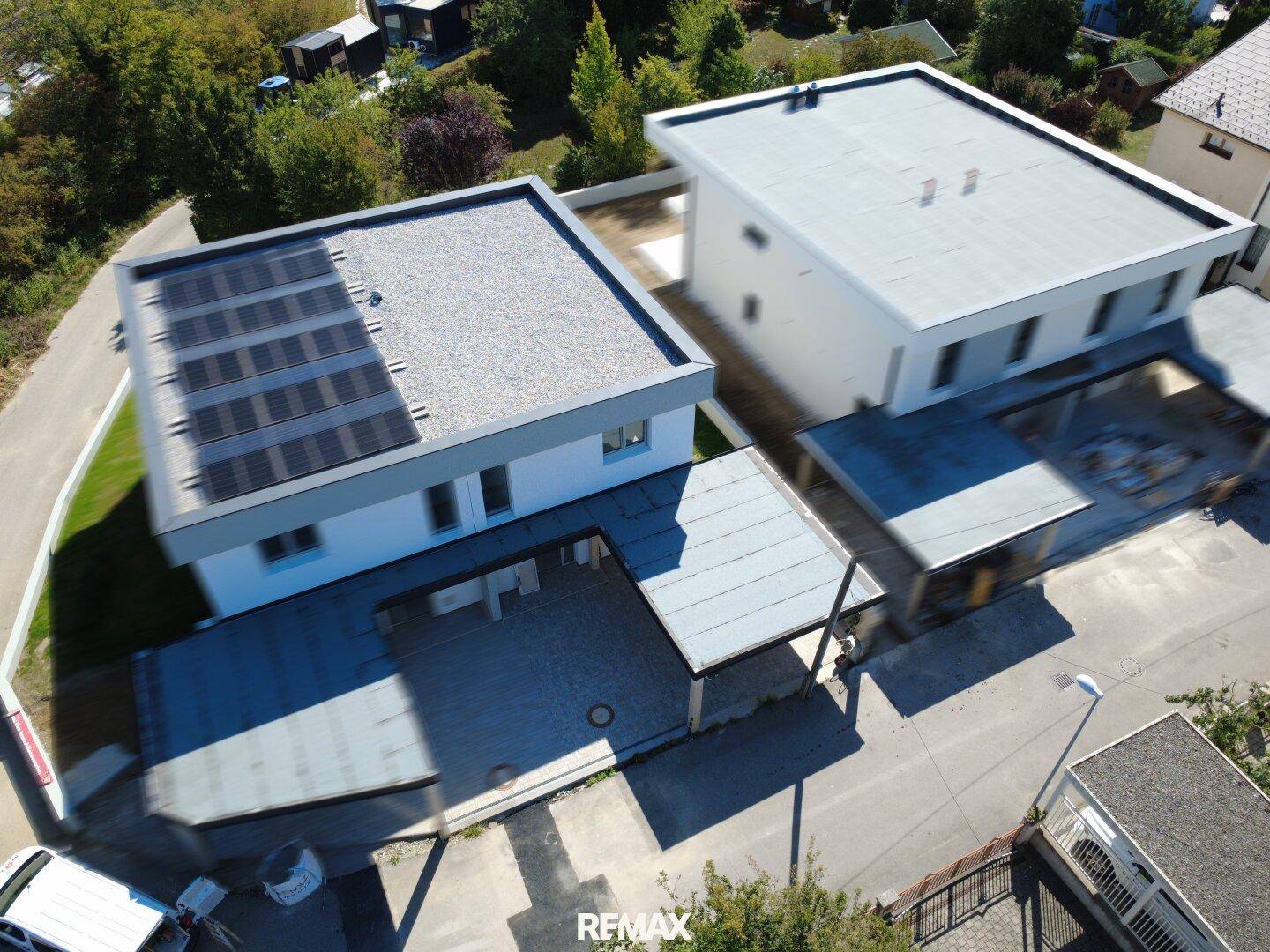 Luftaufnahme von zwei modernen Gebäuden mit Flachdächern und Photovoltaikanlagen.