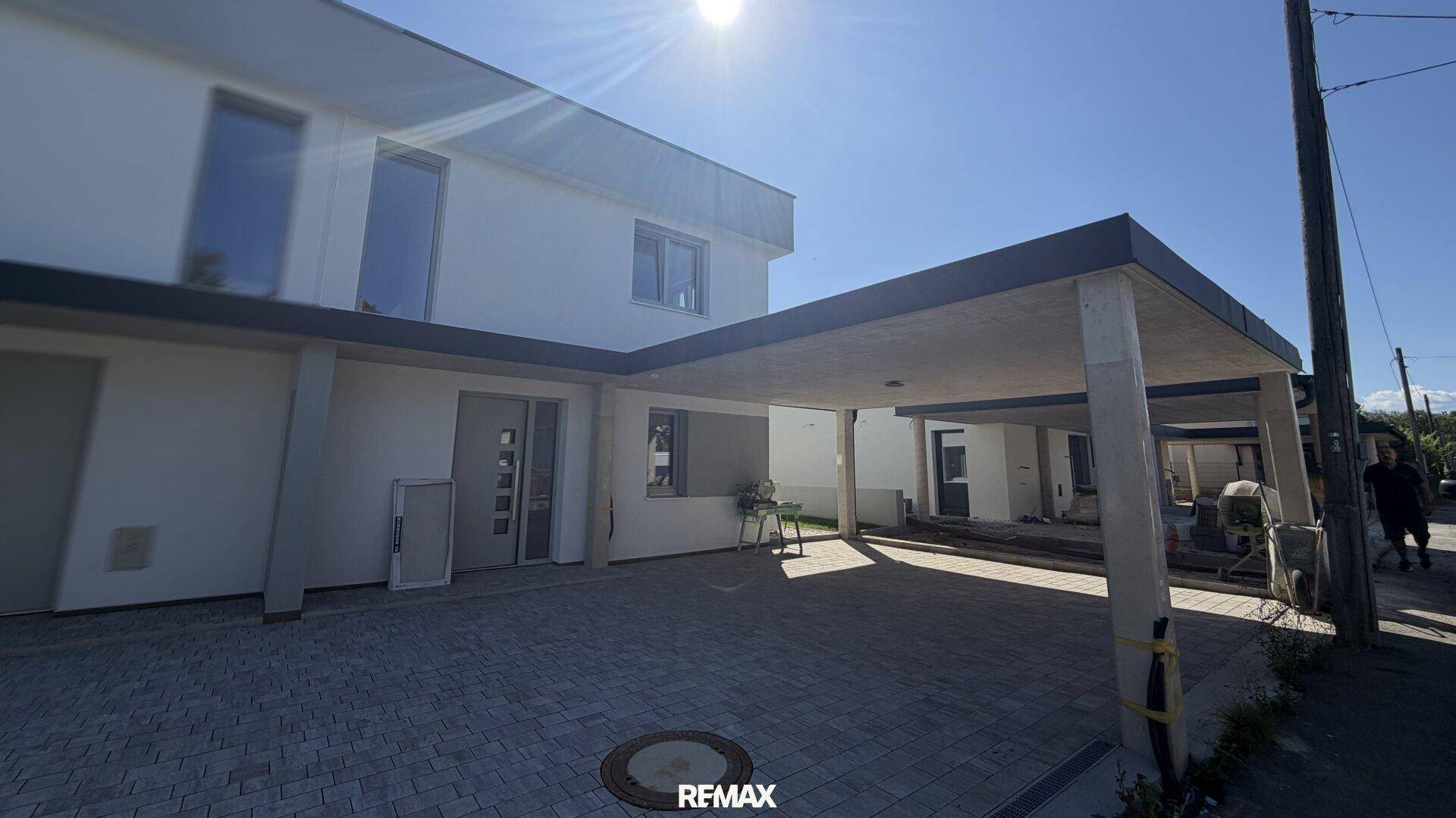 Moderne Hausfassade mit überdachtem Carport und gepflasterter Einfahrt.