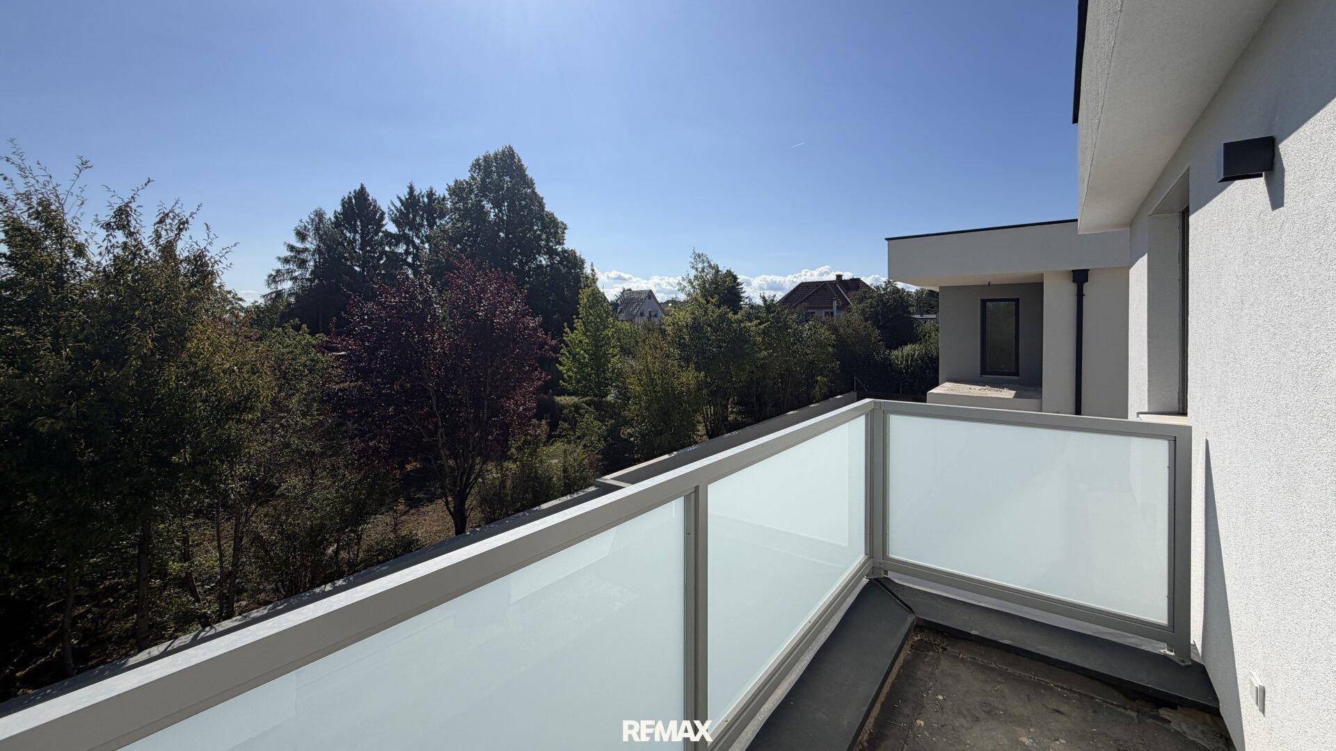 Moderner Balkon mit Glasbrüstung und Blick auf die grüne Umgebung.