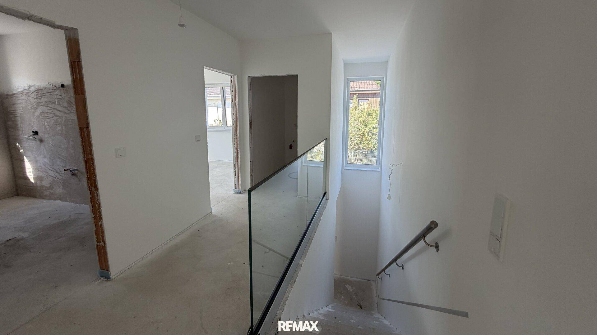 Heller Treppenabsatz mit moderner Glasbrüstung und Blick in den Rohbau.