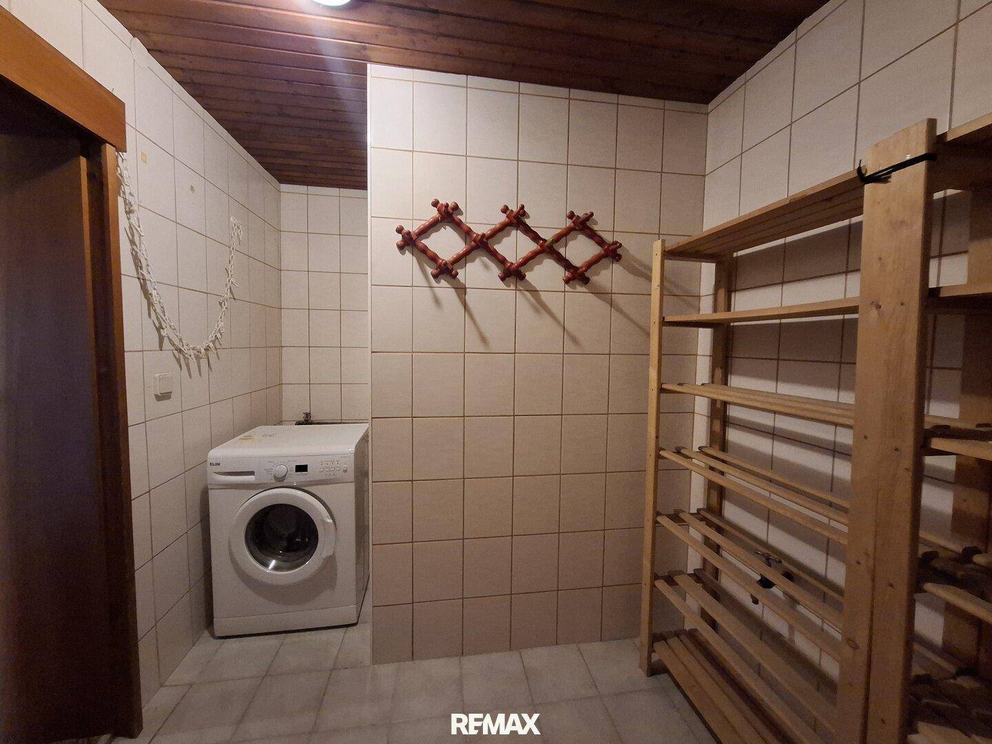 Waschküche mit Waschmaschine, Fliesenboden und Holzregalen für Stauraum.