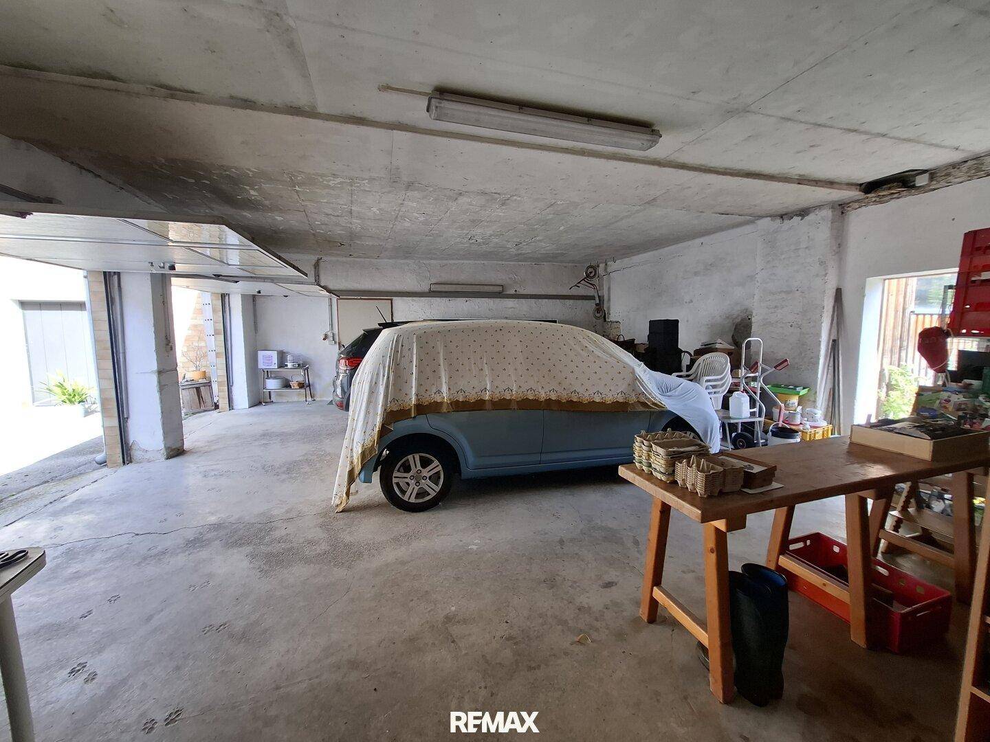 Geräumige Garage mit Betonboden und einem abgedeckten Fahrzeug, die als Abstellfläche dient.