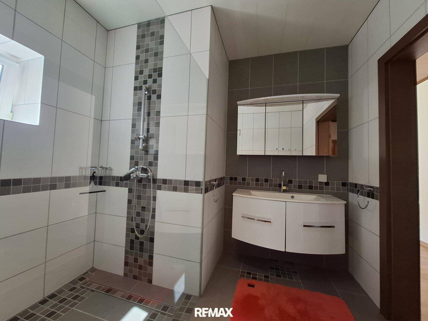 Modern gefliestes Badezimmer mit Duschbereich, Waschbecken und Spiegelschrank.