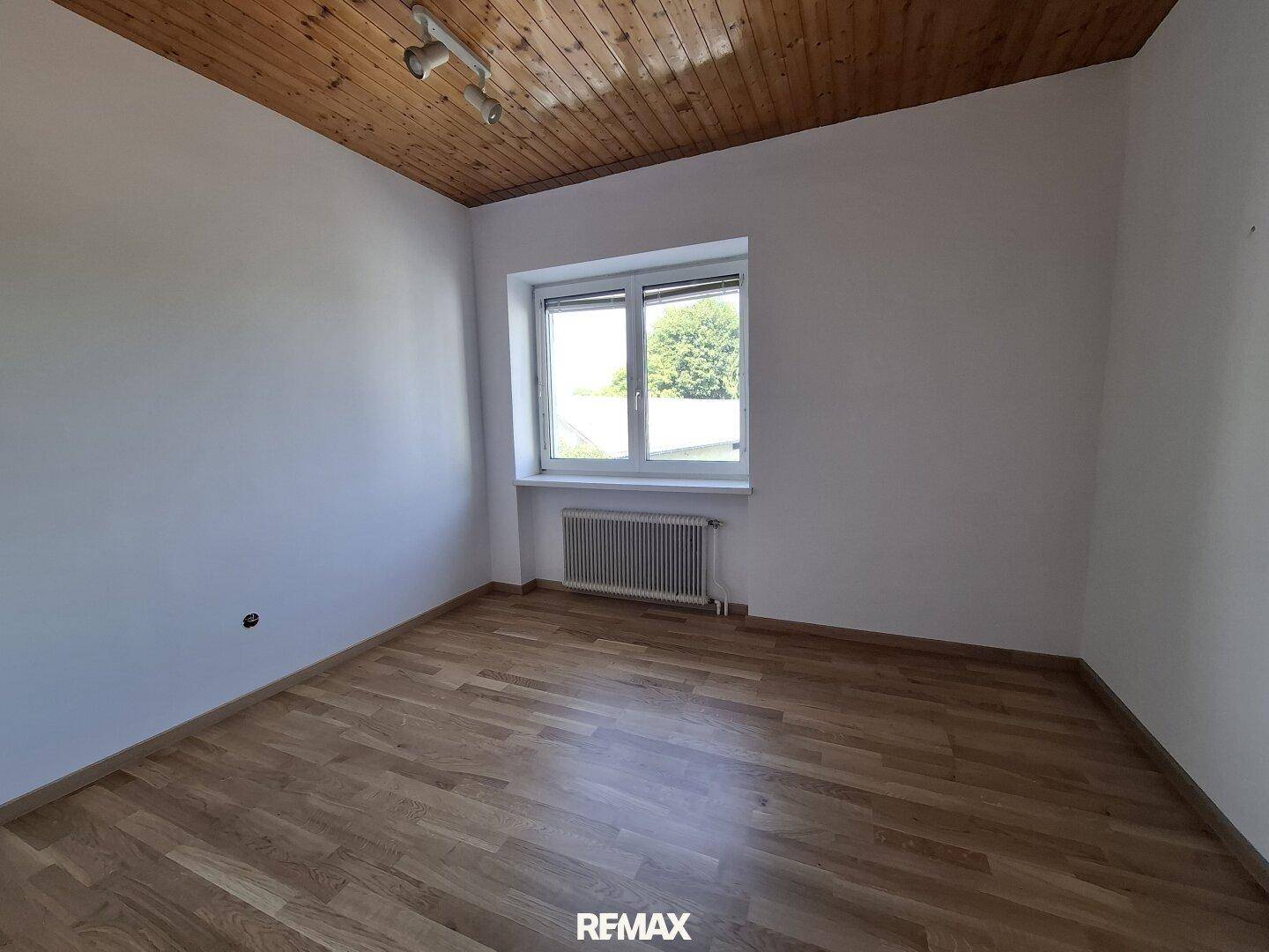 Helles Schlafzimmer mit Holzdecke, Parkettboden und Fenster mit Blick ins Grüne.