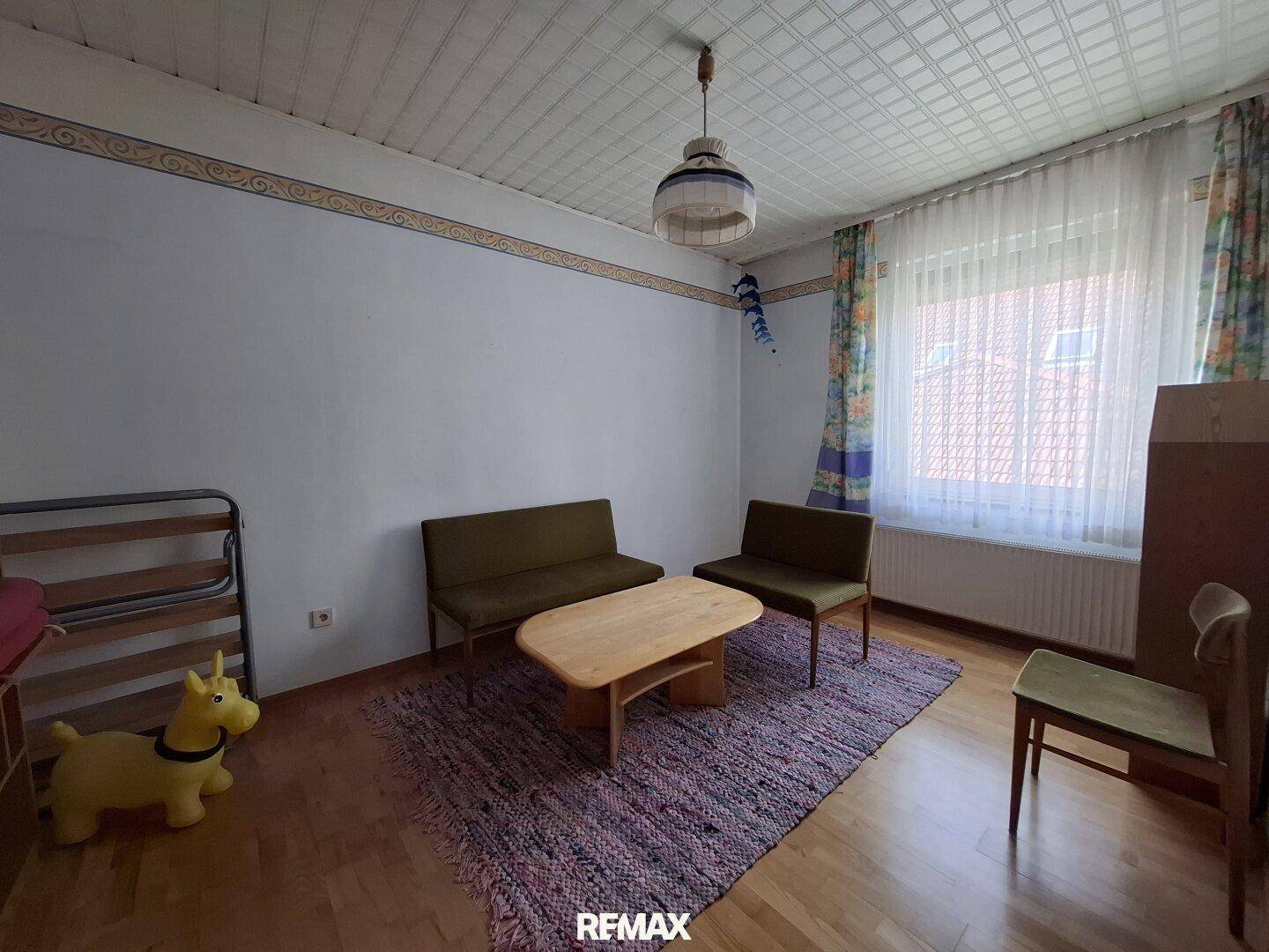 Zimmer mit Parkettboden, kleiner Sitzecke und Fenster, vielseitig nutzbar.
