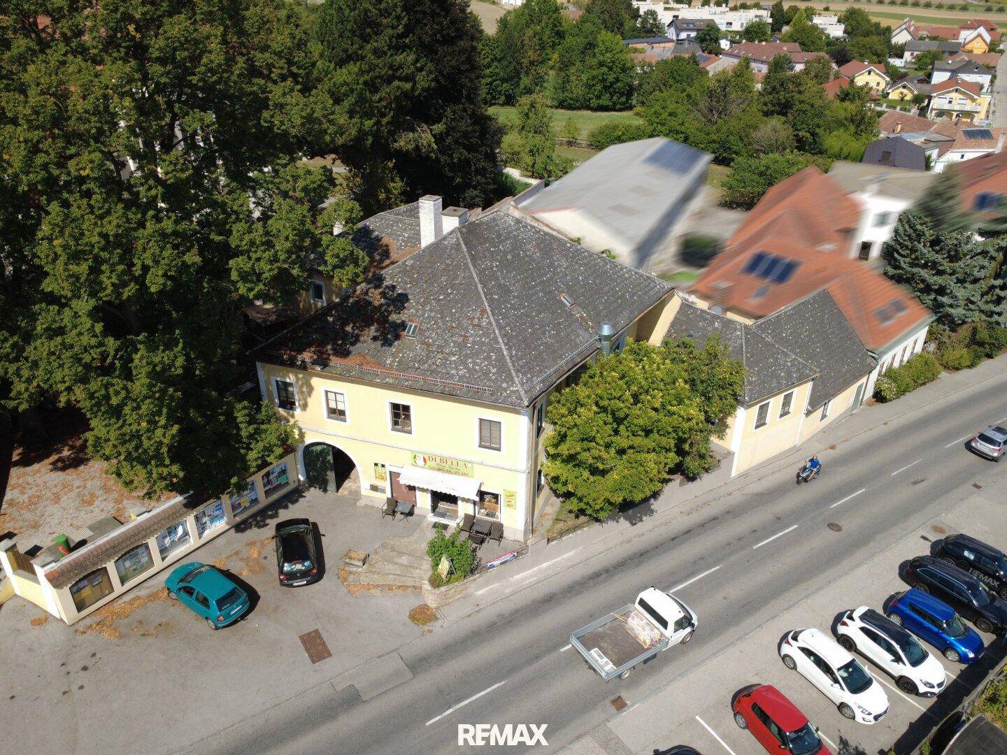 Schrägansicht des gelben Gebäudes mit Pizzeria, Parkplätzen und umliegender Bebauung.