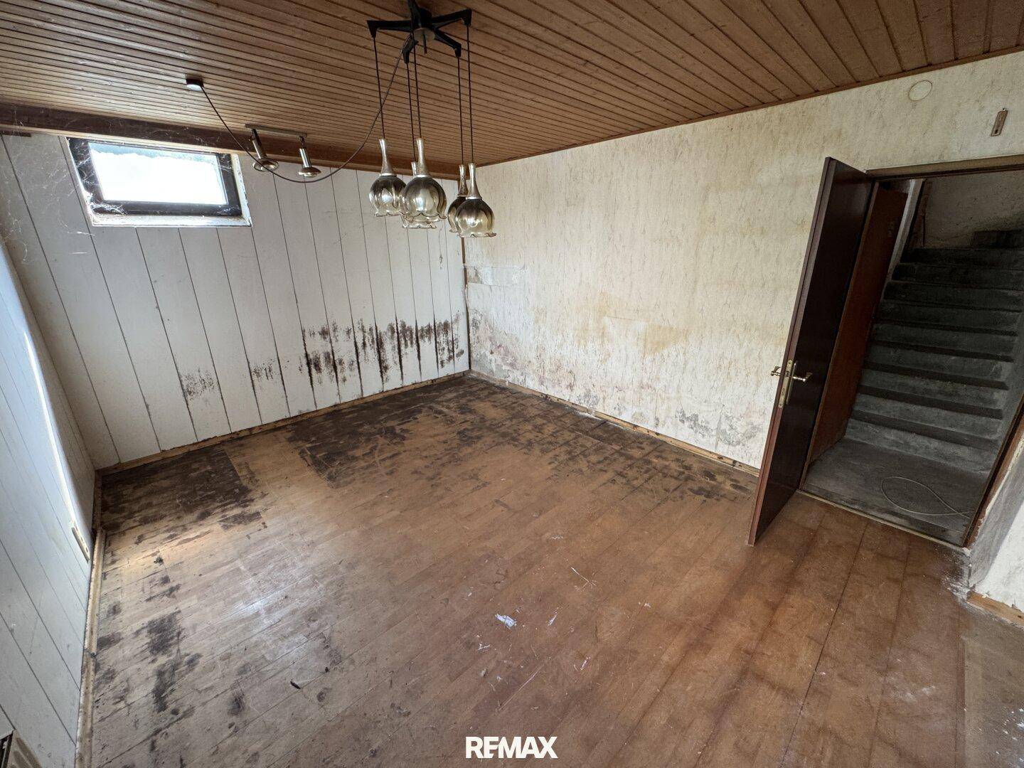 Geräumiges Zimmer mit Holzdecke und Holzboden, zeigt Spuren der Zeit und Renovierungsbedarf.