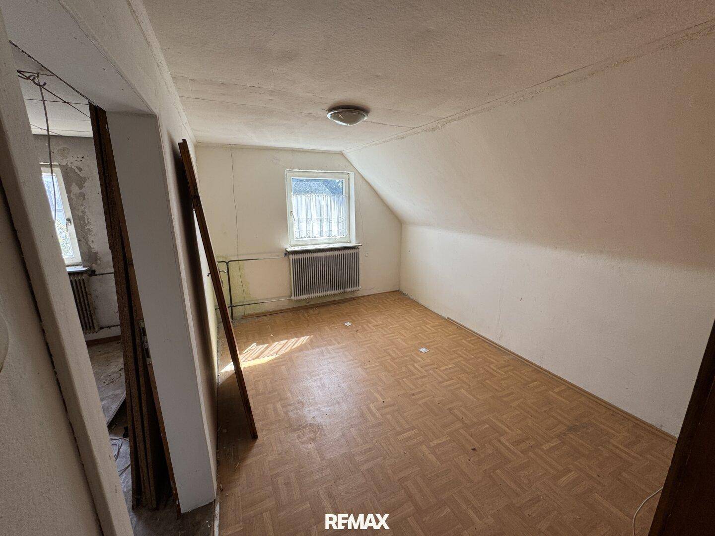 Dachzimmer mit schräger Decke und Parkettboden, bereit für eine persönliche Gestaltung.