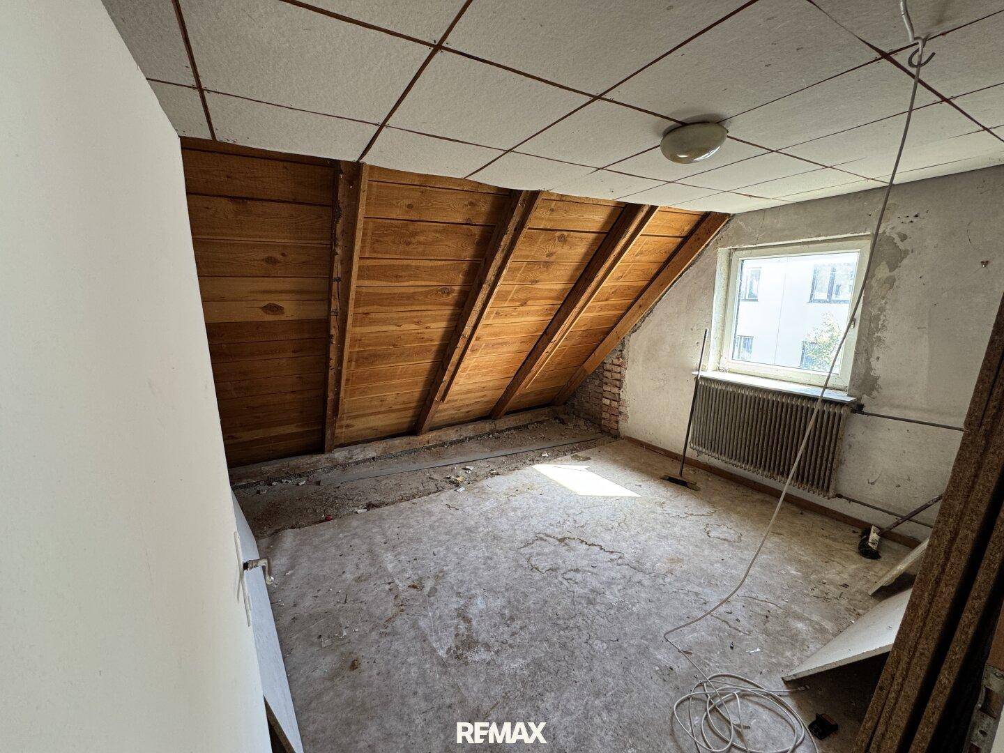 Dachzimmer im Rohzustand mit sichtbaren Holzbalken und Betonboden, ideal für Renovierung.