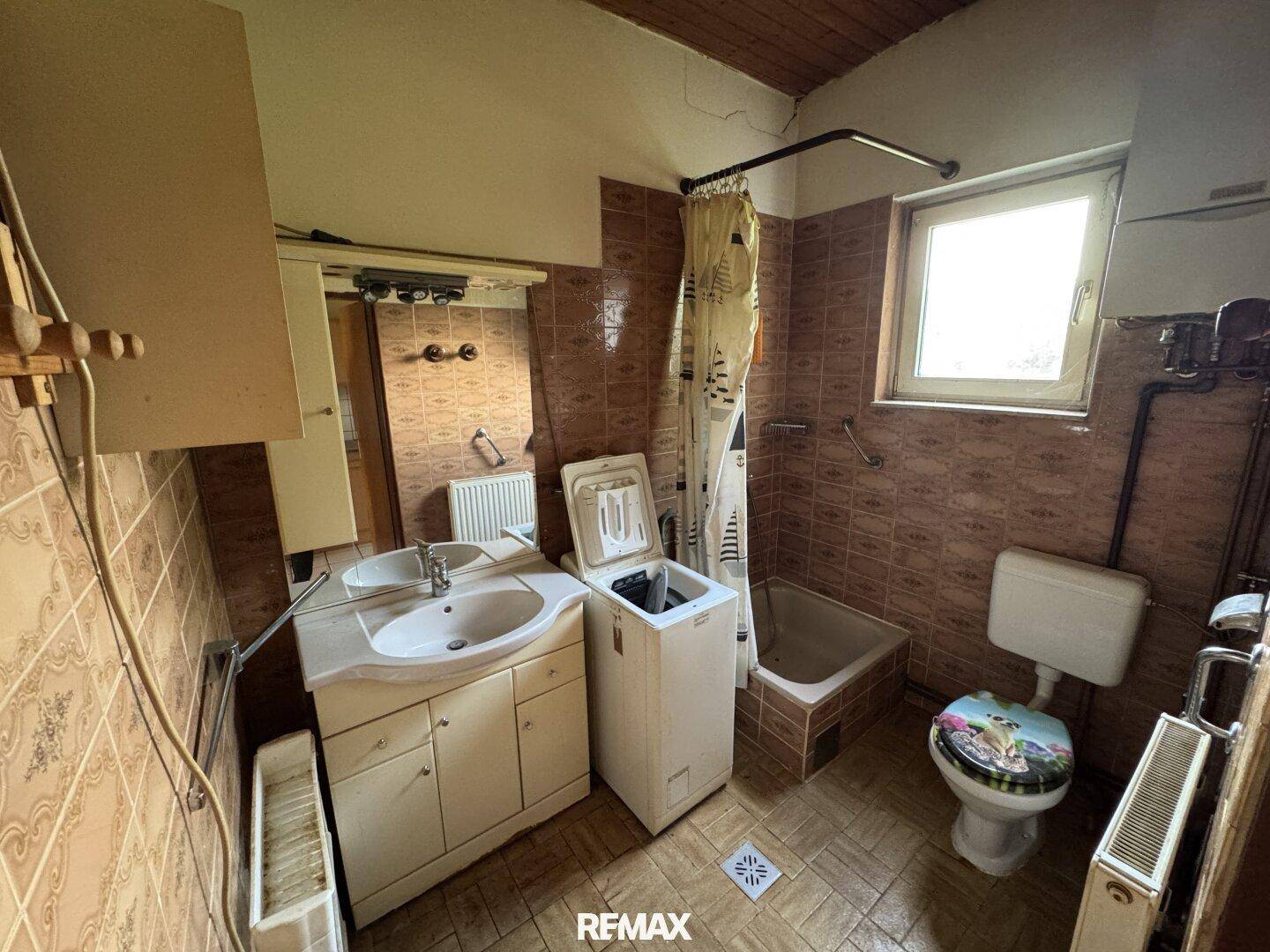 Badezimmer im 80er-Jahre-Stil mit Badewanne, Waschbecken und Waschmaschine, renovierungsbedürftig.