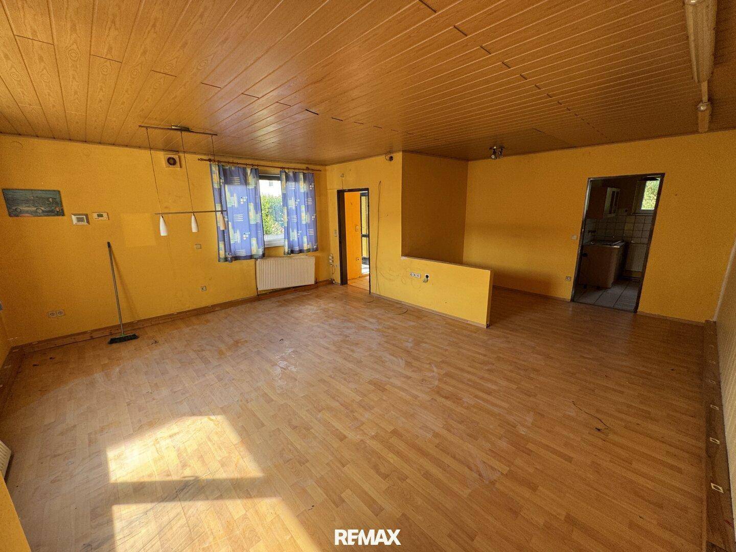 Großes Wohnzimmer mit gelben Wänden, Holzdecke und Parkettboden, hell und geräumig.