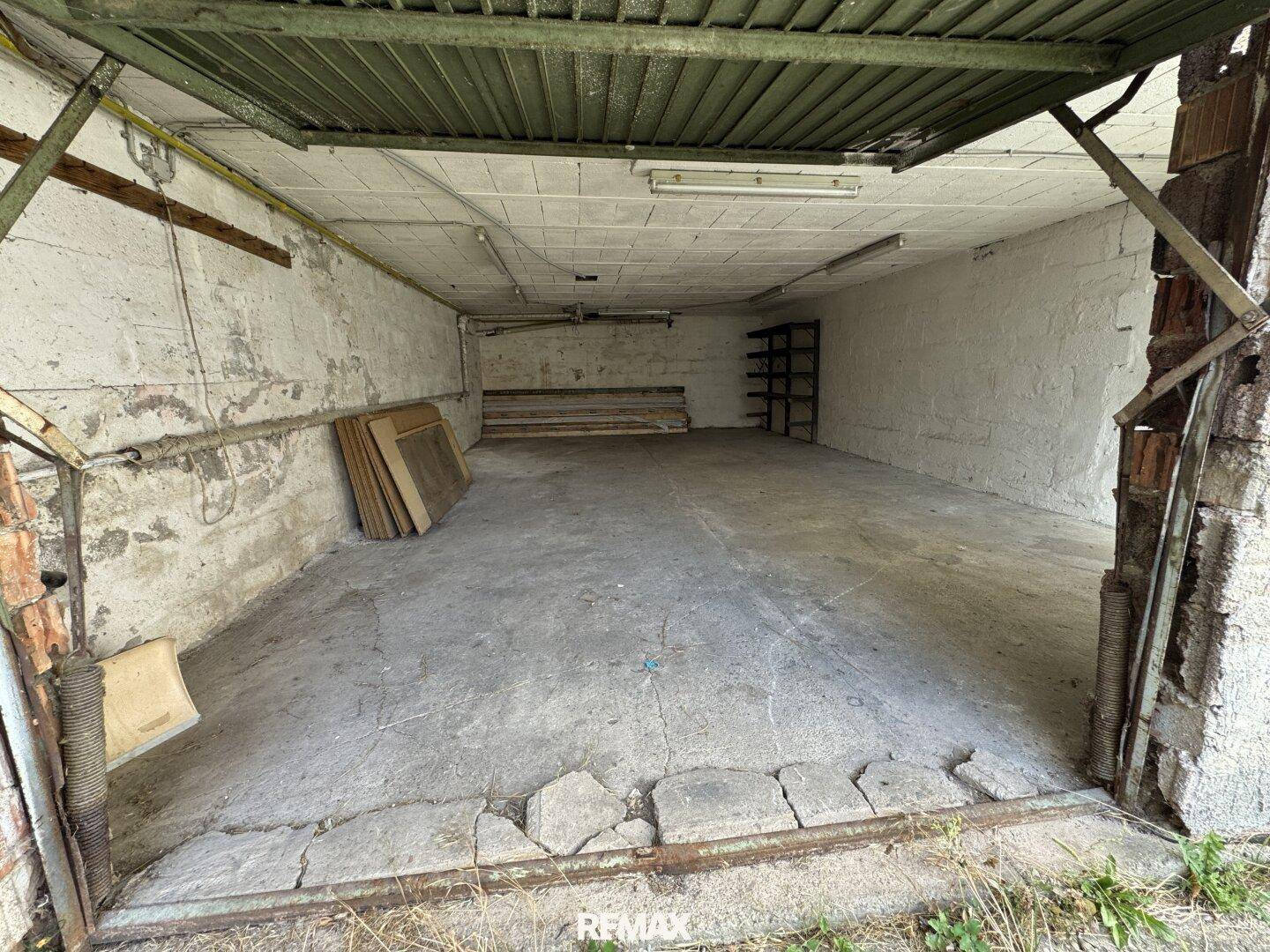 Geräumige Garage mit Betonboden und altem Garagentor, bietet Platz für Fahrzeuge und Lagerung.
