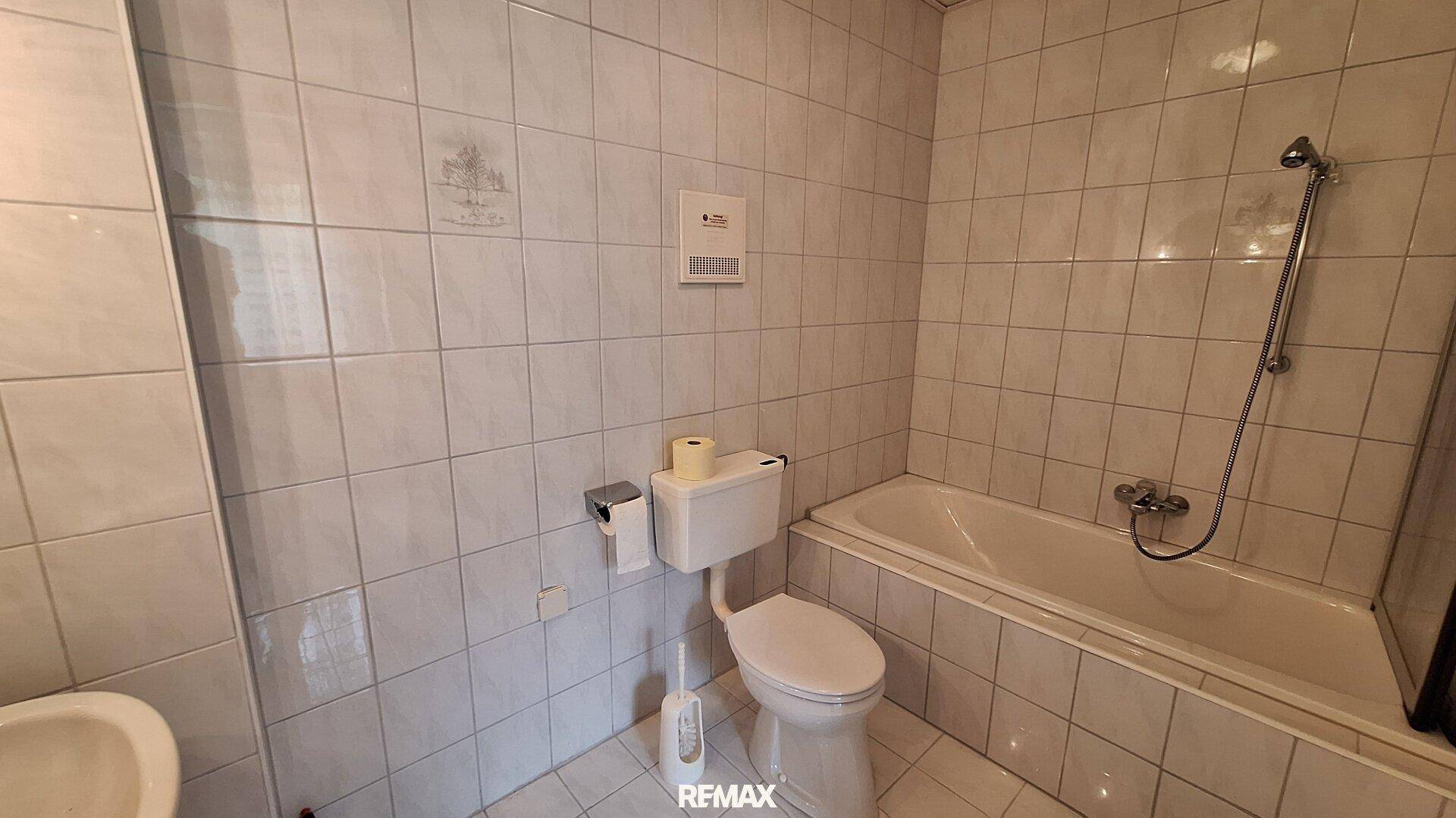 Badezimmer mit Badewanne, WC und weißen Fliesen an Wänden und Boden.