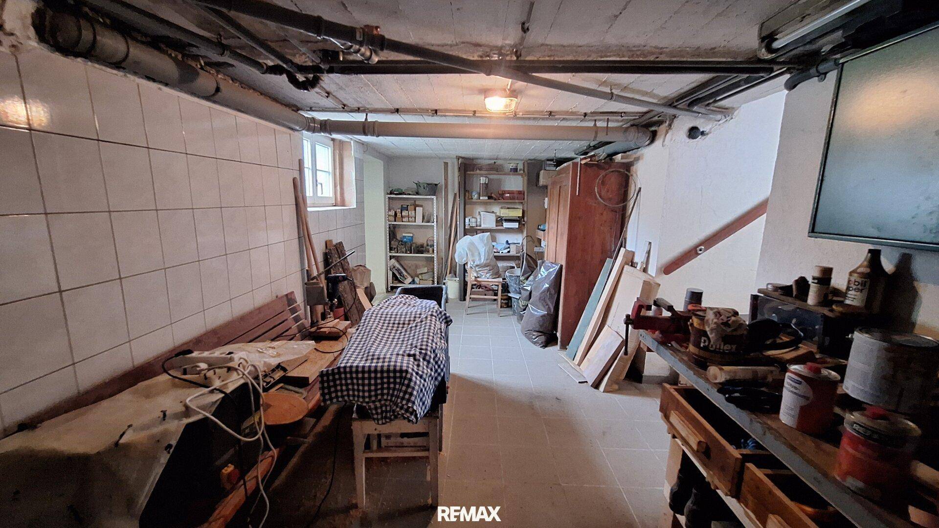 Kellerraum als Werkstatt und Lagerfläche mit sichtbaren Rohren und Fenster.