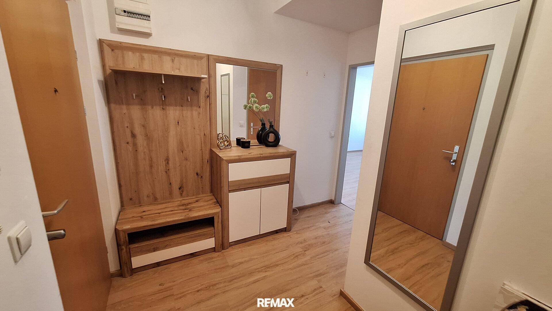 Einladender Eingangsbereich mit moderner Garderobe, großem Spiegel und Laminatboden in Holzoptik.
