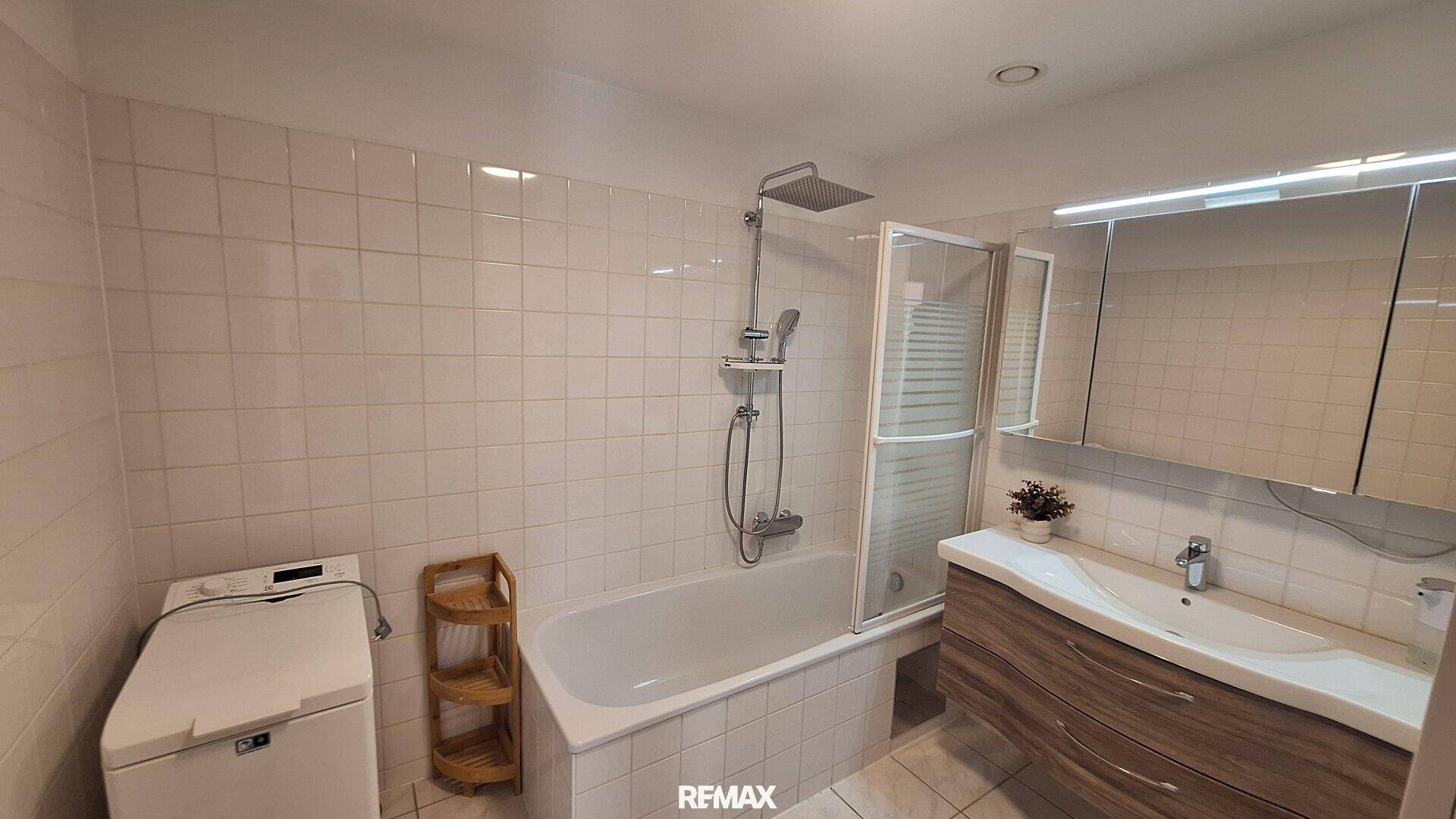 Helles Badezimmer mit Badewanne, integrierter Dusche, Waschmaschine und Spiegelschrank.