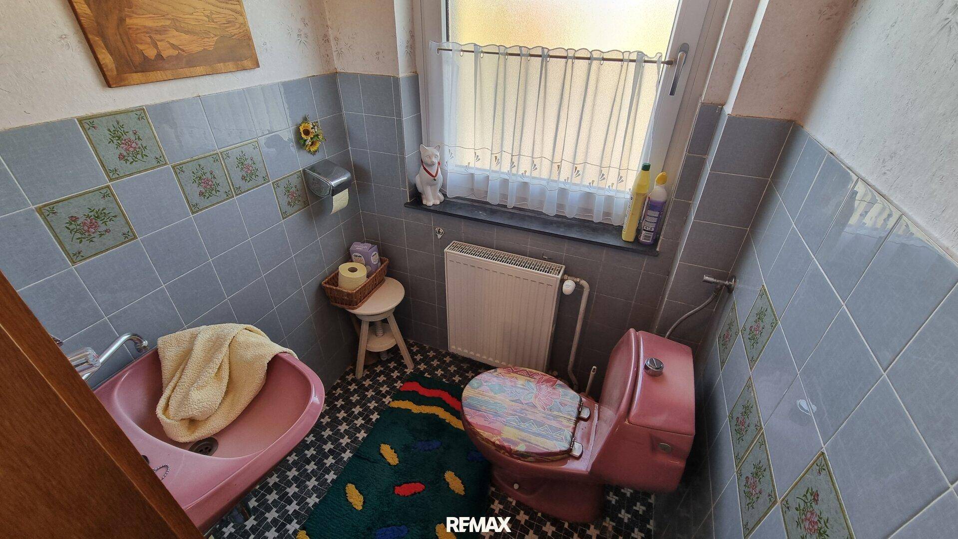 Separate Toilette im Stil der 80er Jahre mit rosa WC und Waschbecken, sowie Fenster.