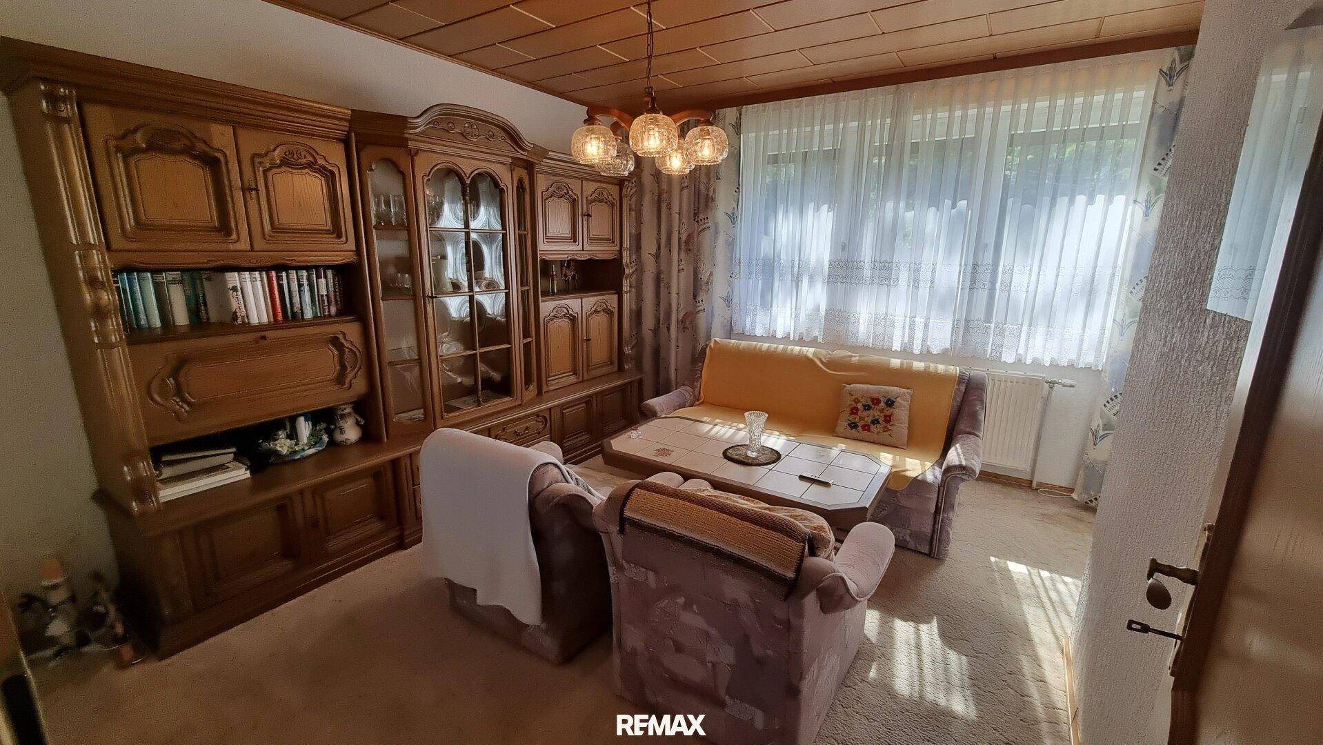 Wohnzimmer mit traditionellen Holzmöbeln, Sofa und Sesseln, sowie großen Fenstern.