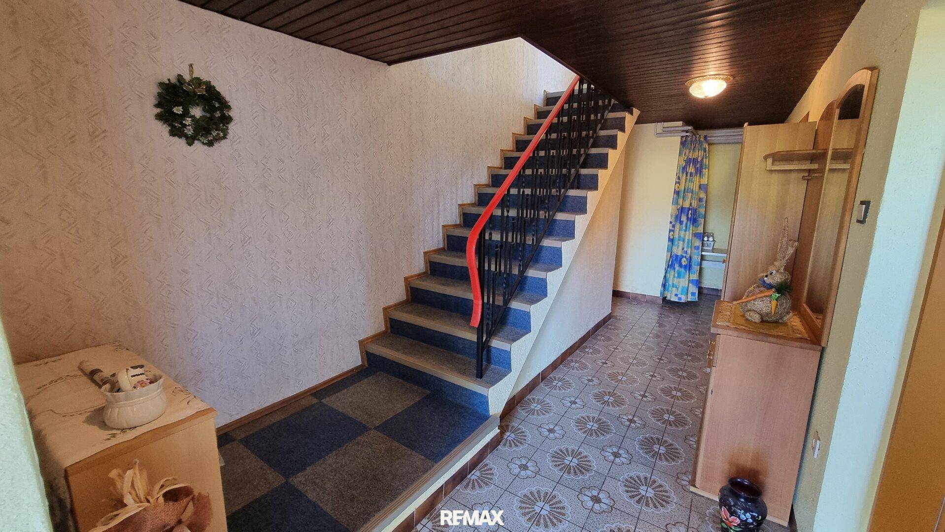 Flur mit gemusterten Fliesen, Holztreppe und schmiedeeisernem Geländer, führt in die obere Etage.