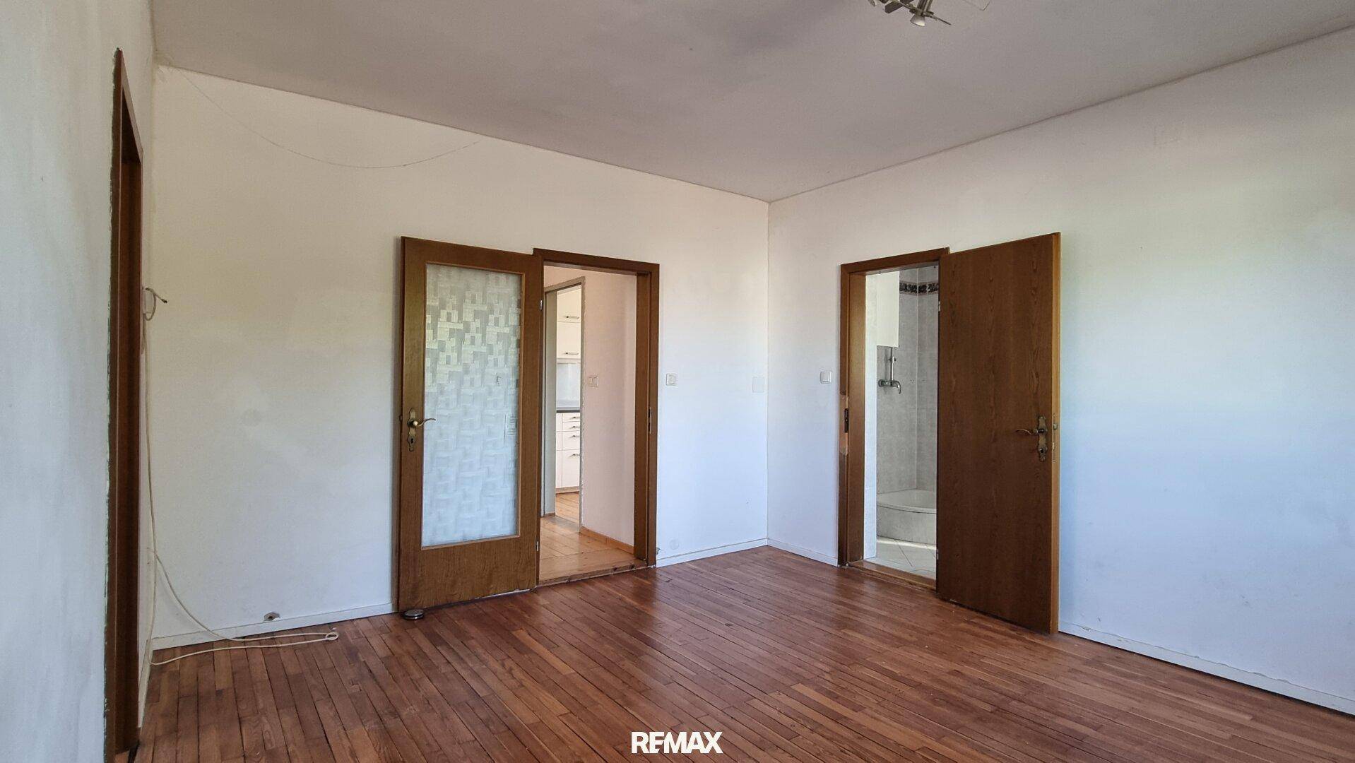 Leerer Raum mit Holzboden und zwei Türen, eine davon führt in ein Badezimmer.