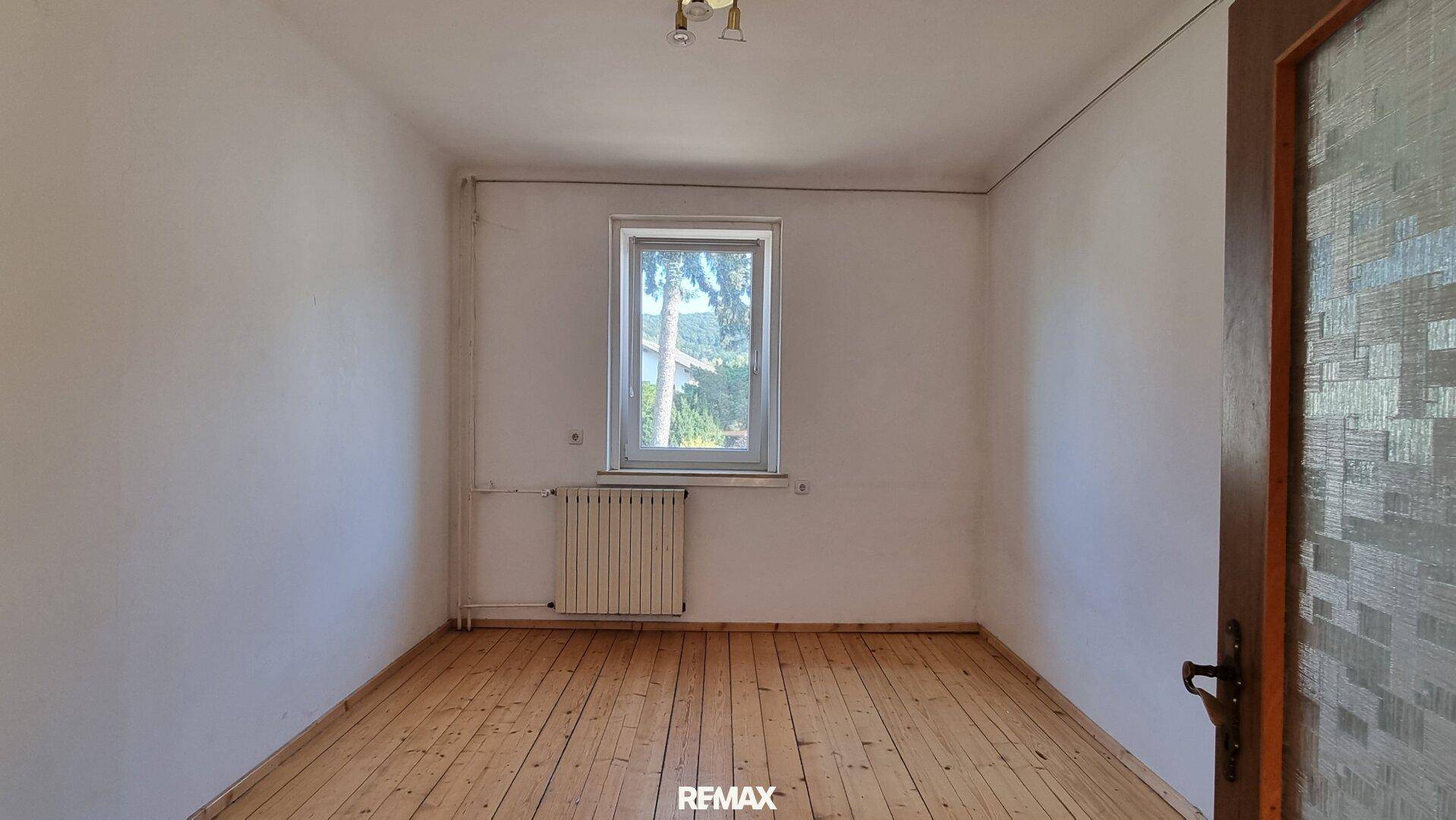 Einfaches Zimmer mit Holzdielenboden und einem Fenster, das Tageslicht hereinlässt.