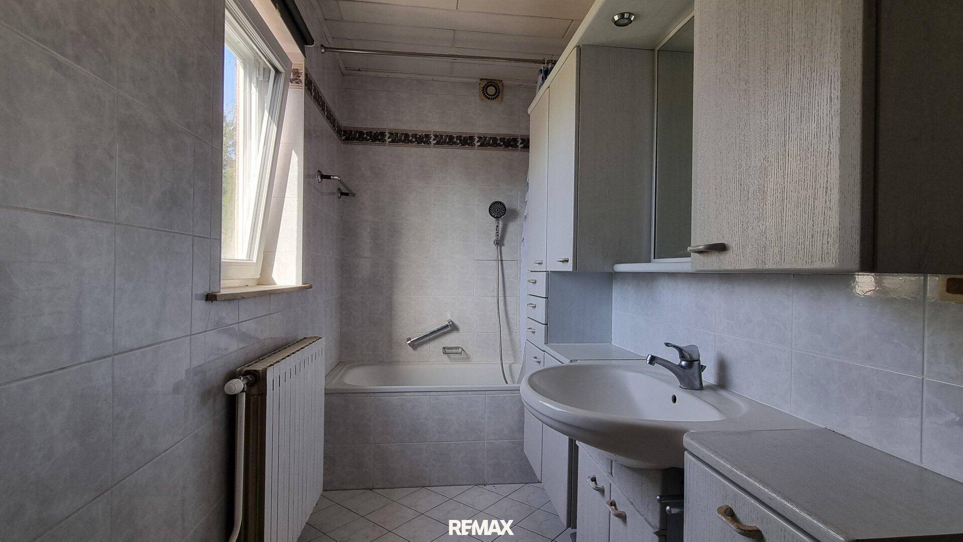 Gefliestes Badezimmer mit Badewanne, Waschbecken und einem Fenster für natürliche Belüftung.