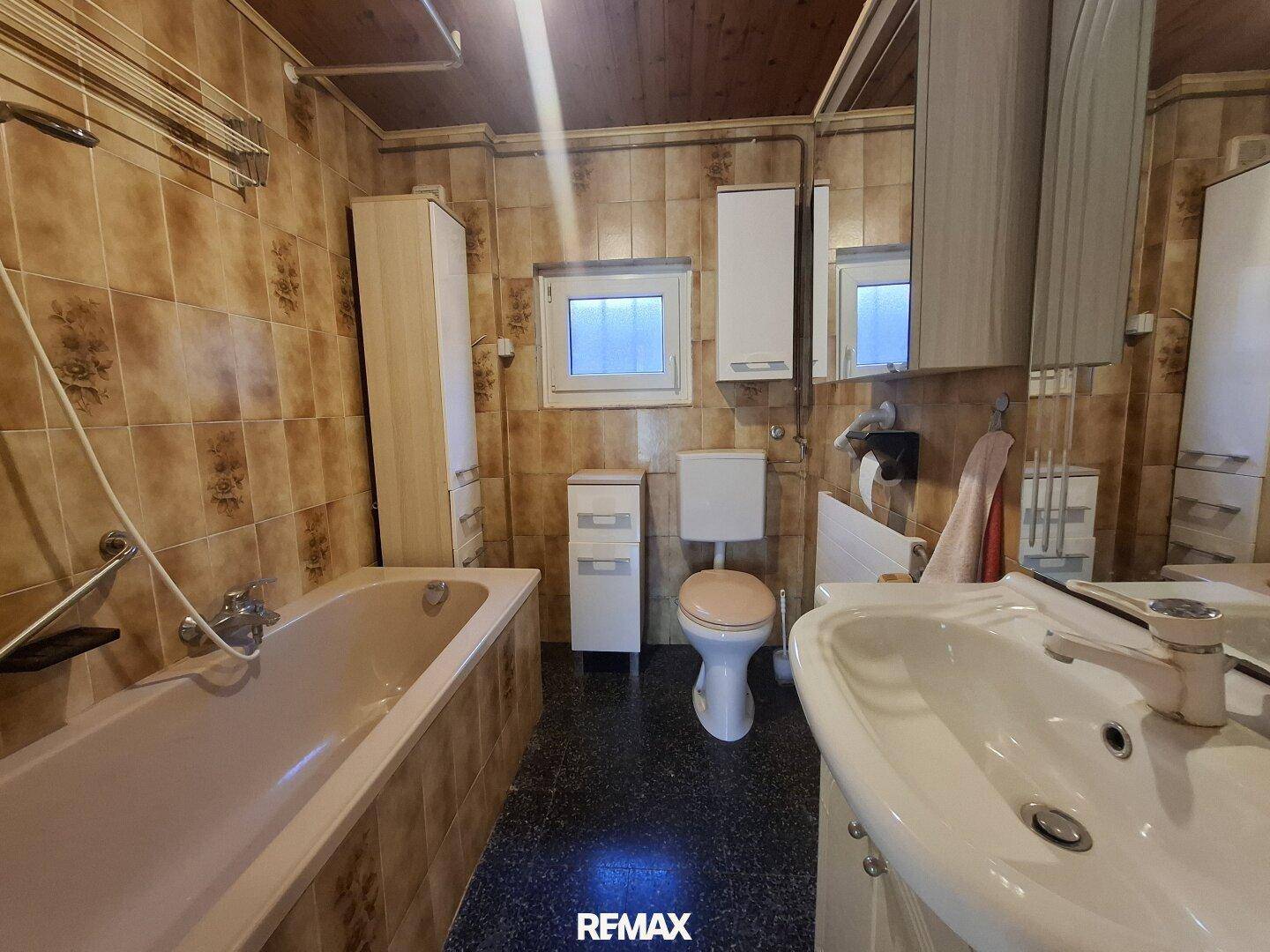 Badezimmer mit Badewanne, Waschbecken und WC, ausgestattet mit braunen Wand- und Bodenfliesen.