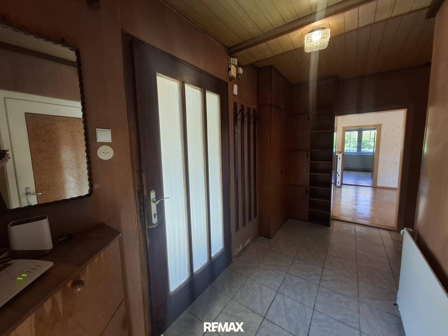 Eingangsbereich mit Fliesenboden, Holzdecke und Garderobe, führt zu weiteren Räumen im Haus.