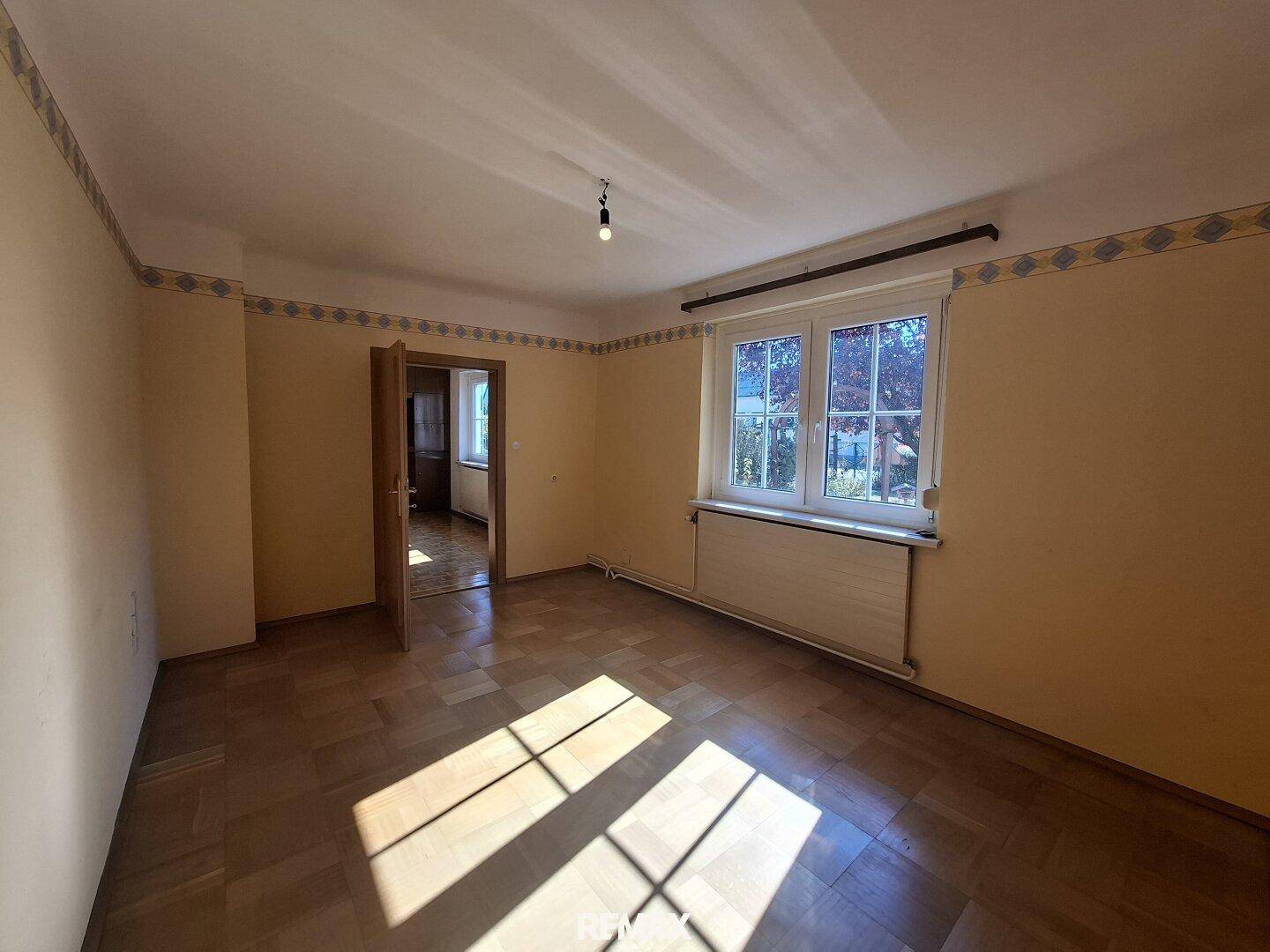 Helles Zimmer mit Parkettboden und gelben Wänden, bietet viel natürliches Licht durch das Fenster.
