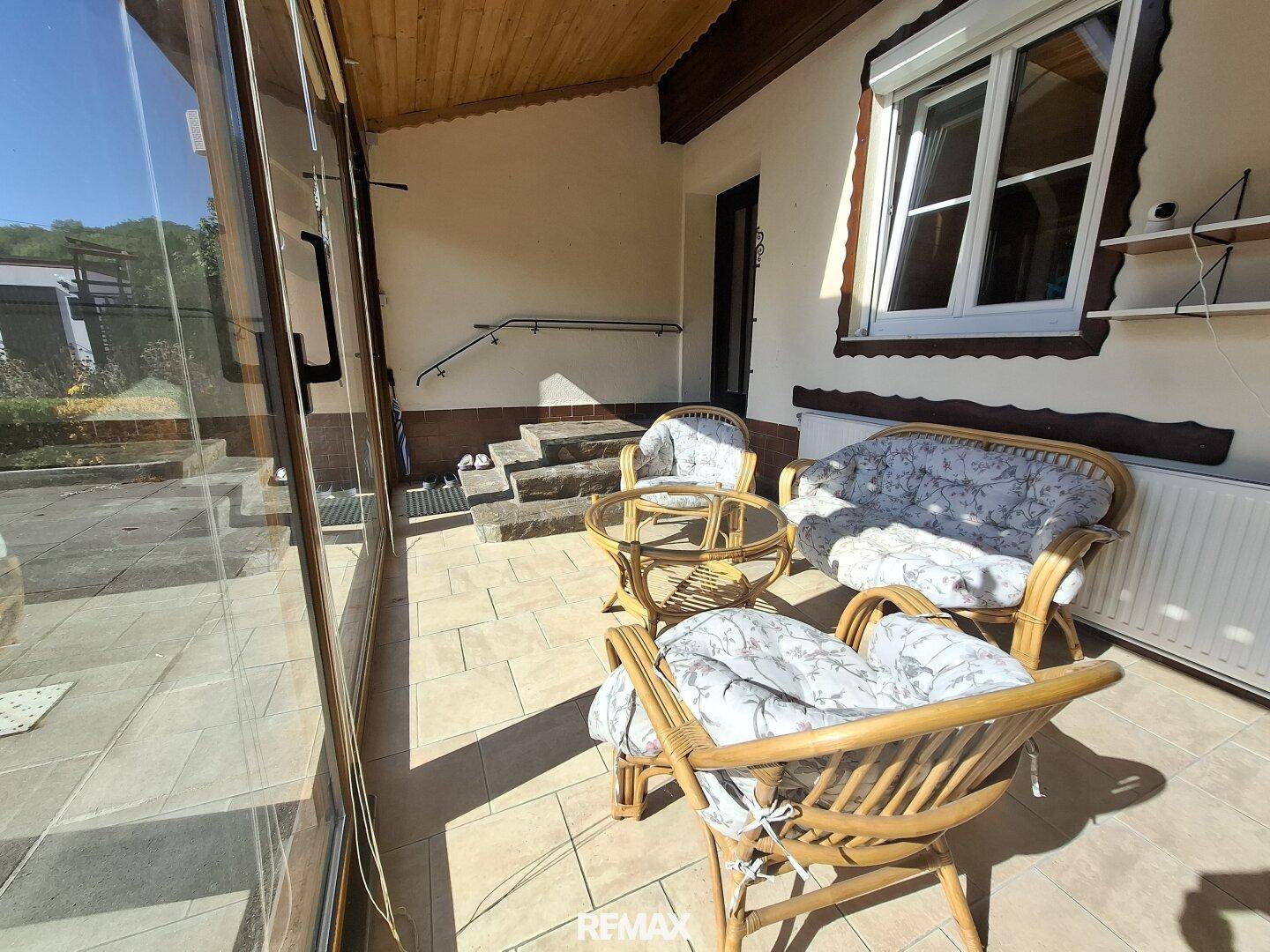 Überdachter Außenbereich mit Rattanmöbeln und Zugang zum Garten über eine kleine Treppe.
