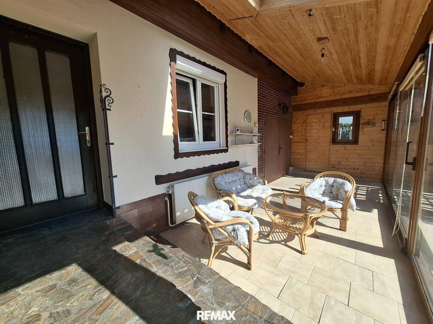 Gemütlicher überdachter Außenbereich mit Rattanmöbeln und Fliesenboden, ideal zum Entspannen im Freien.