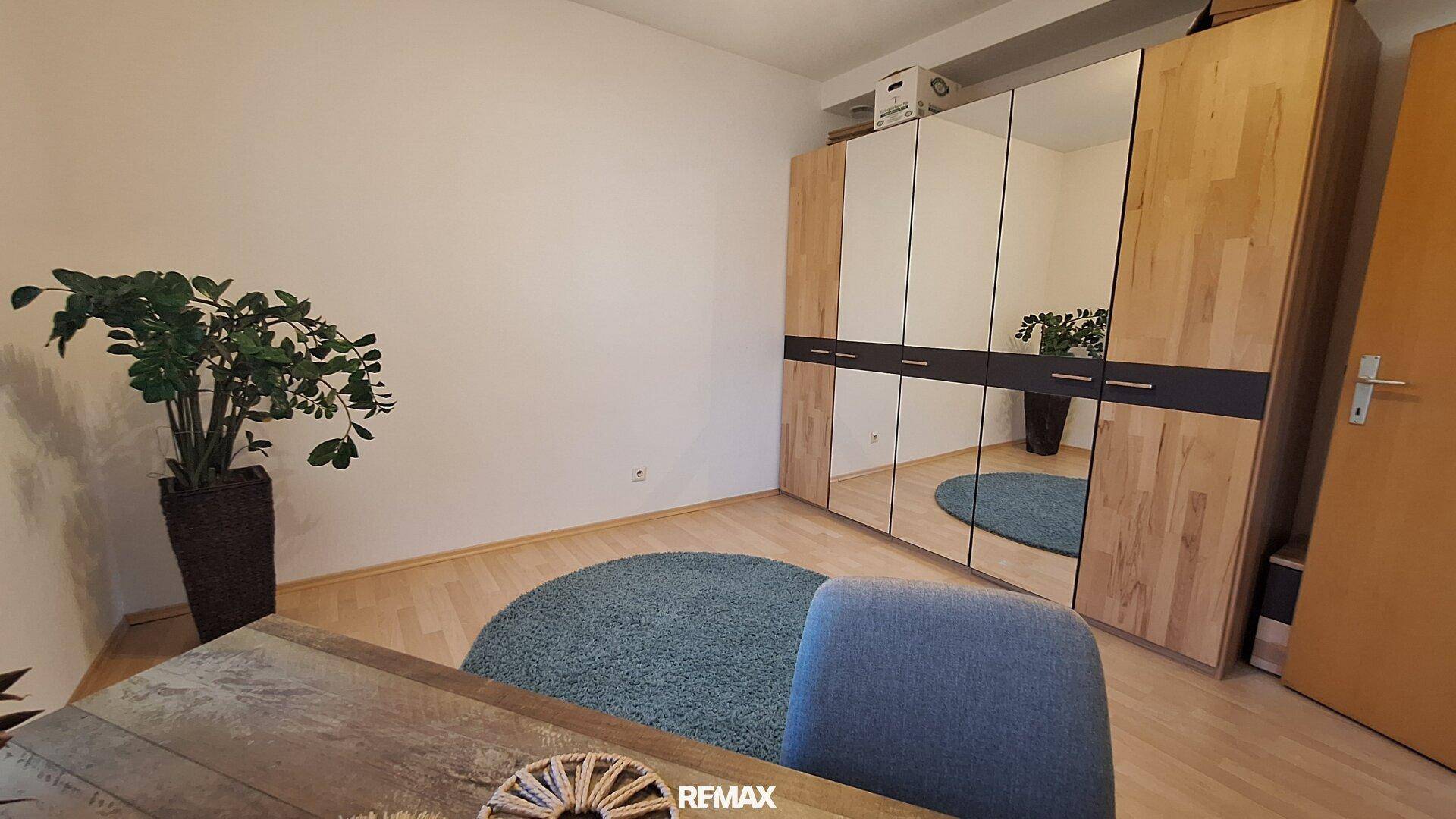 Schlafzimmer mit großem Spiegelschrank, Laminatboden und schlichtem Design.