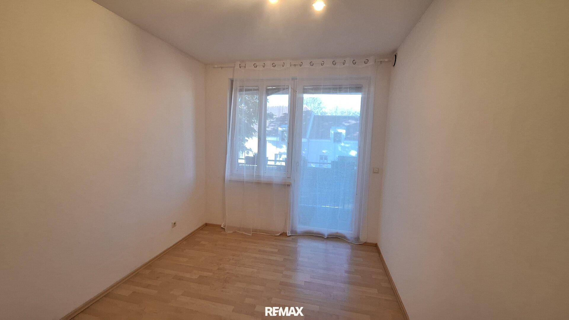 Helles Zimmer mit Laminatboden und Zugang zu einem Balkon.