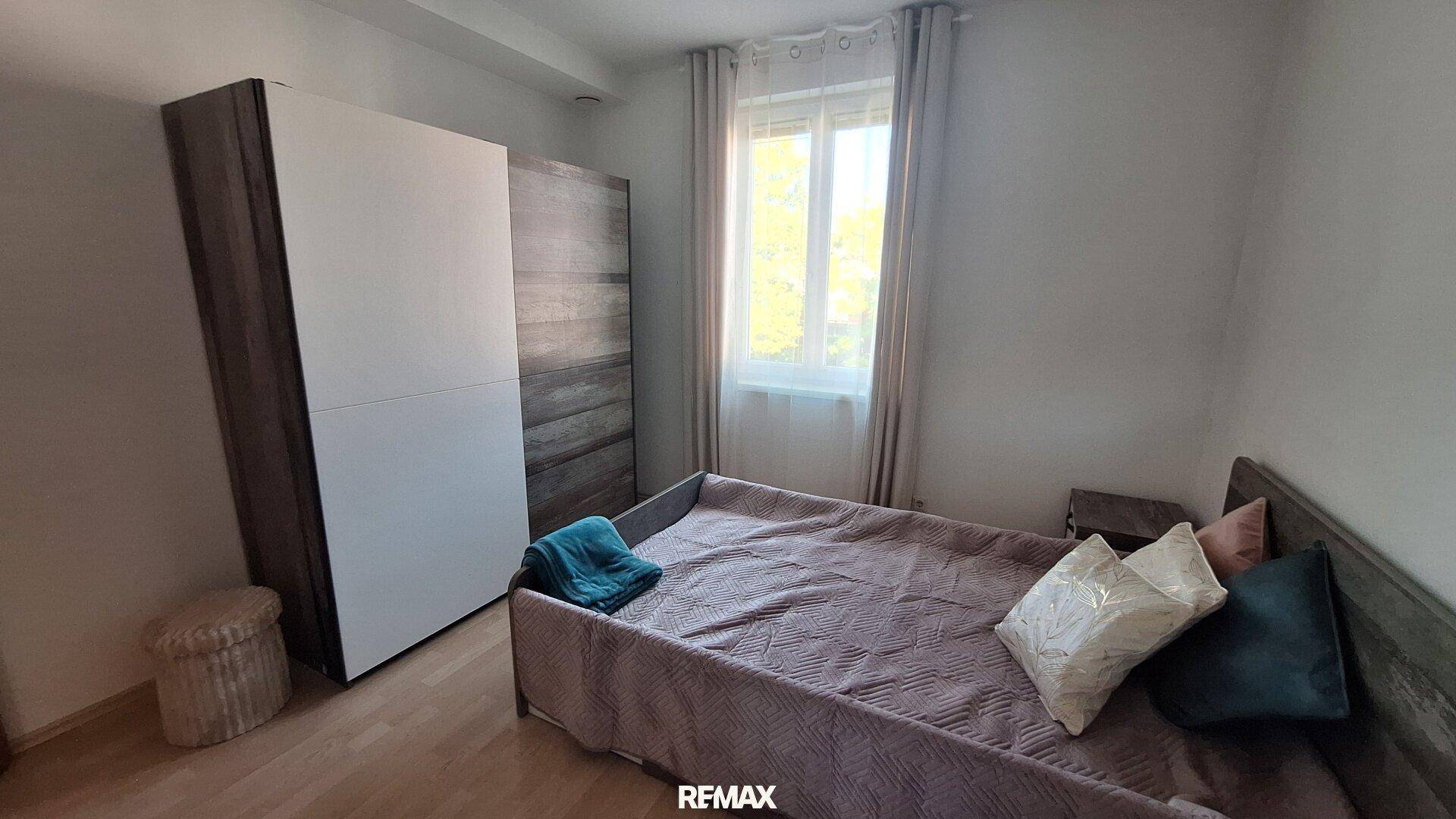 Schlafzimmer mit Doppelbett, Kleiderschrank und hellem Fenster.