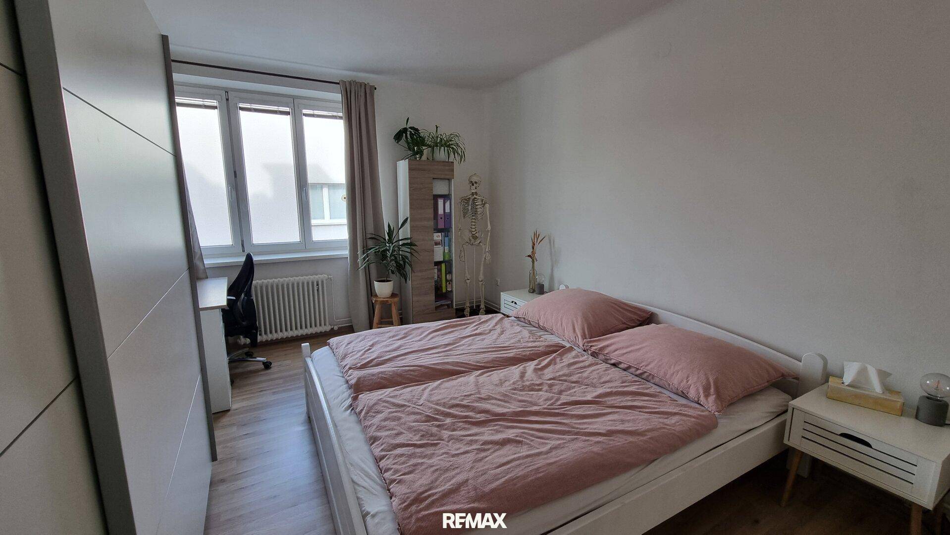 Gemütliches Schlafzimmer mit Doppelbett, Schreibtisch am Fenster und hellem Parkettboden.