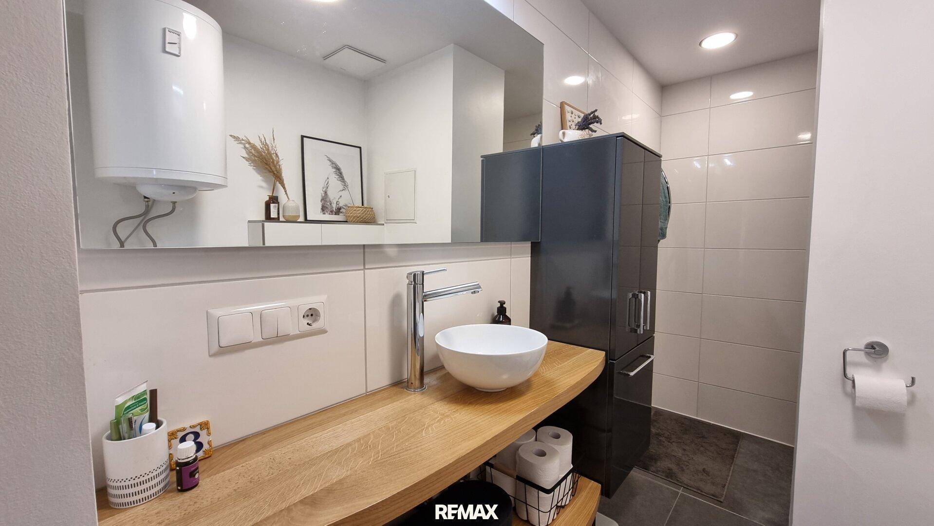 Modernes Badezimmer mit Waschtisch, großem Spiegel und weiß gefliesten Wänden.